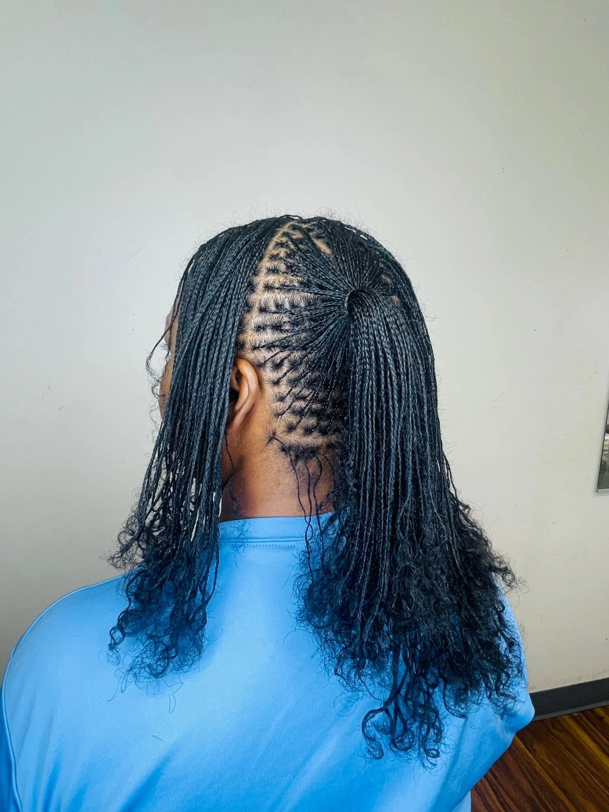 Back view of a woman with braided hairstyles, including a circular braid pattern on top and long, curly hair.