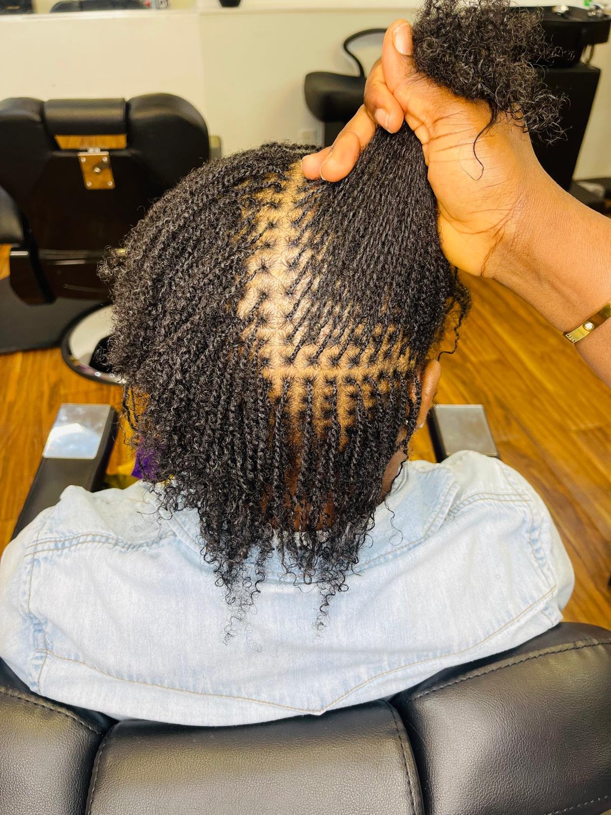 Person with natural hair having twists installed, seated in a salon chair with a stylist's hand in their hair.
