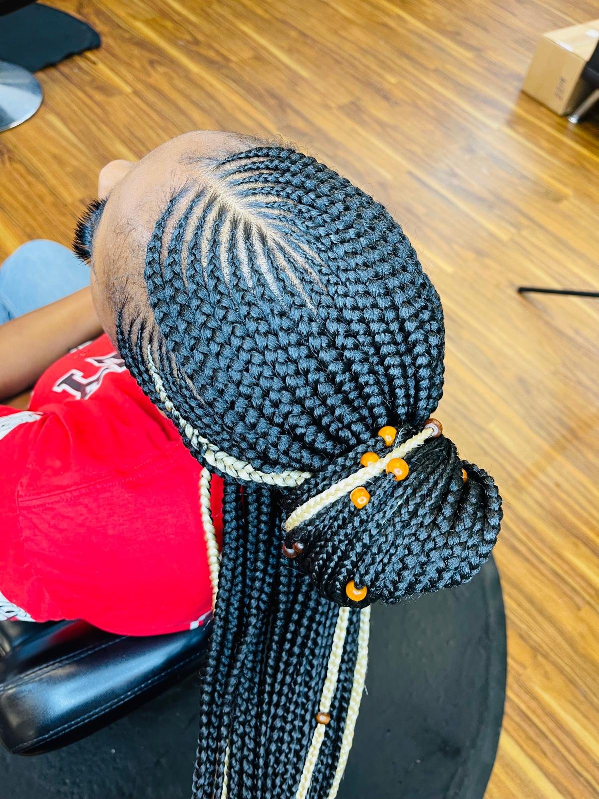 A person with long, black braided hair decorated with orange and cream beads. The braids are styled into a high bun on top of the head.