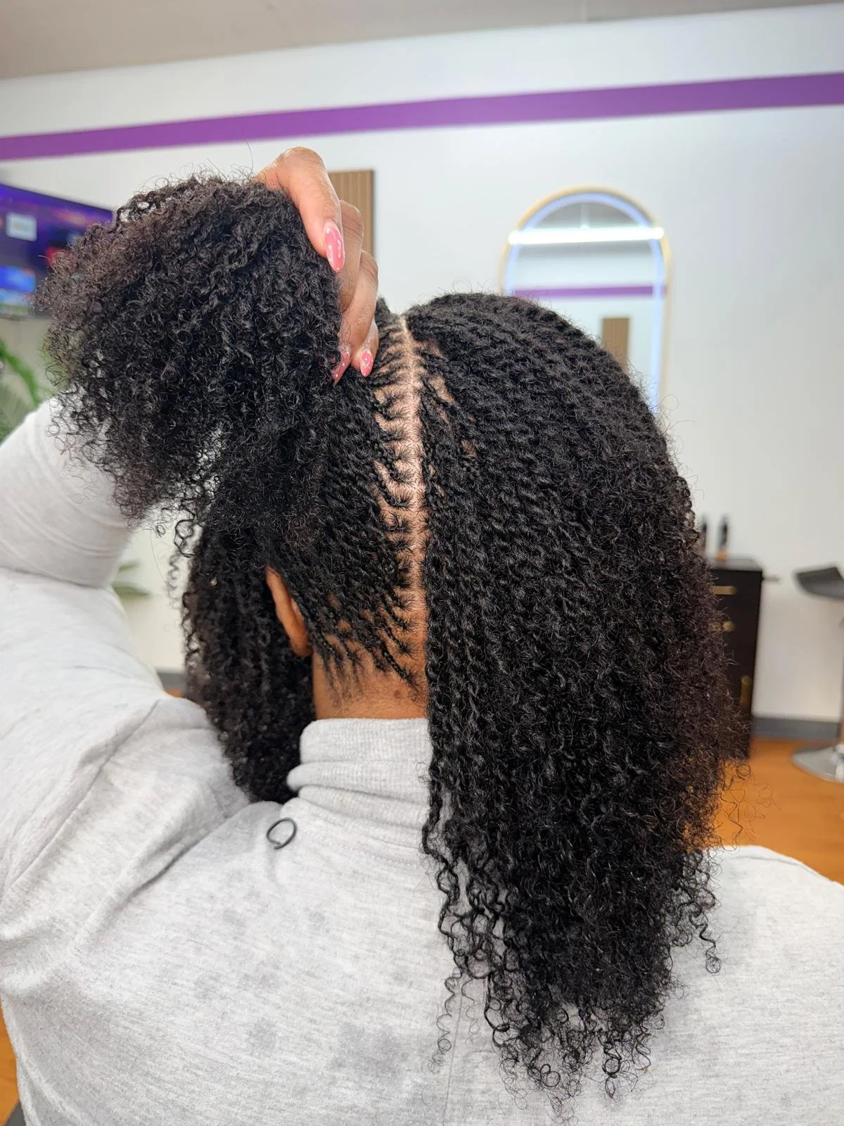 A woman with braided hair is getting her hair styled in a salon. The stylist is holding a section of her hair, preparing to style it.
