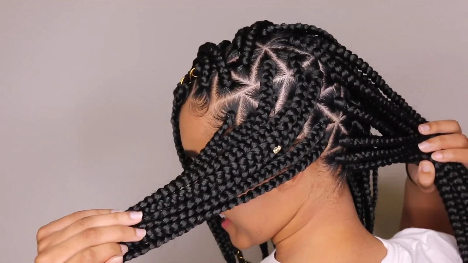 Woman with neatly styled braided hair, adjusting her braids, with gold accessories in her hair.