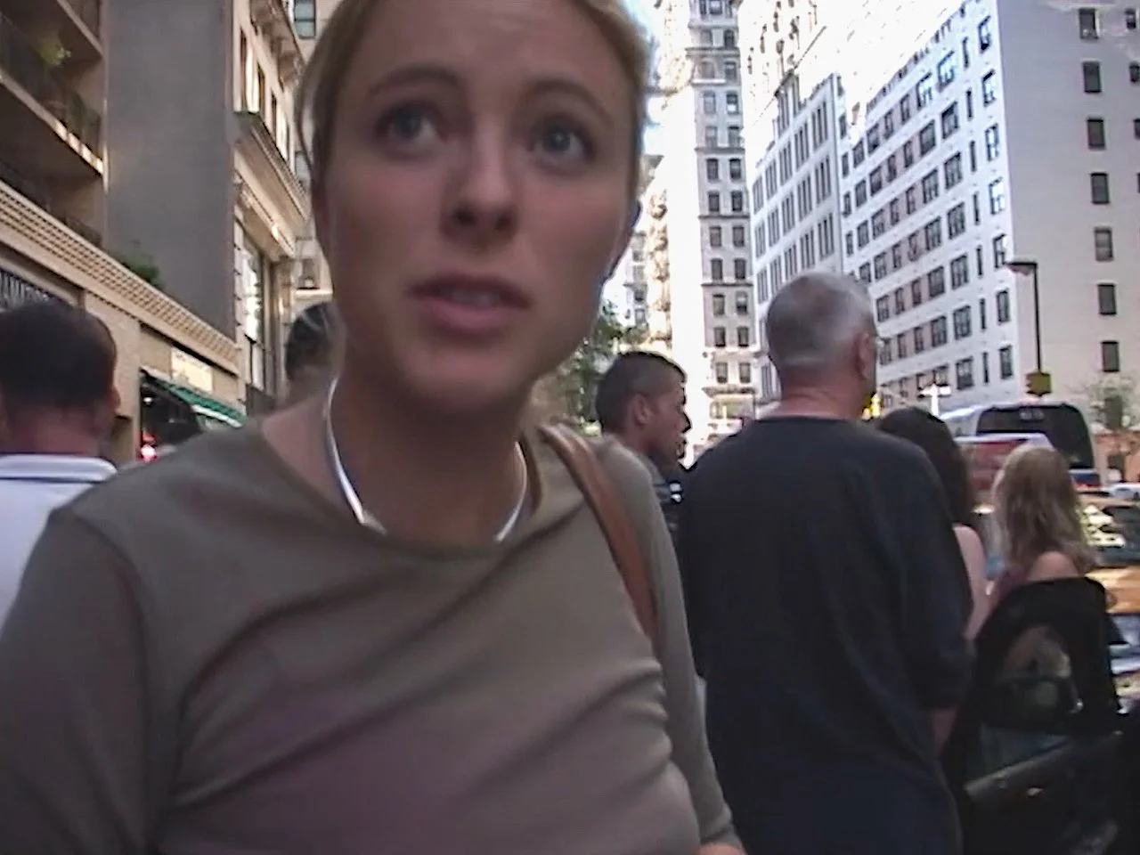 A woman talking to someone outdoors in an urban setting surrounded by other people and tall buildings.