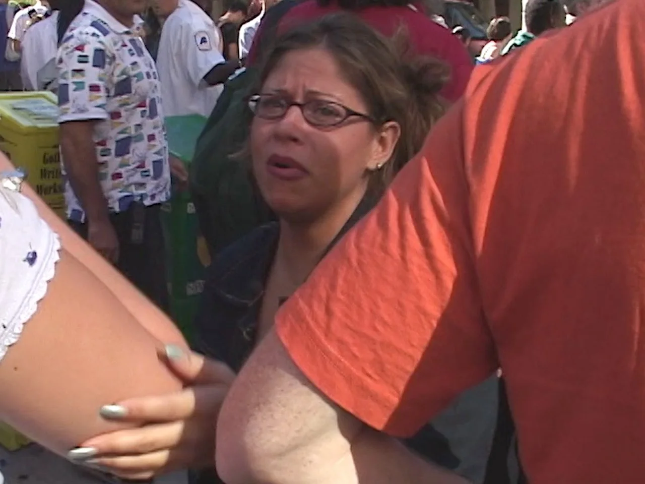 A woman with glasses and short brown hair in a crowd, appearing to be engaged in a public event or gathering.