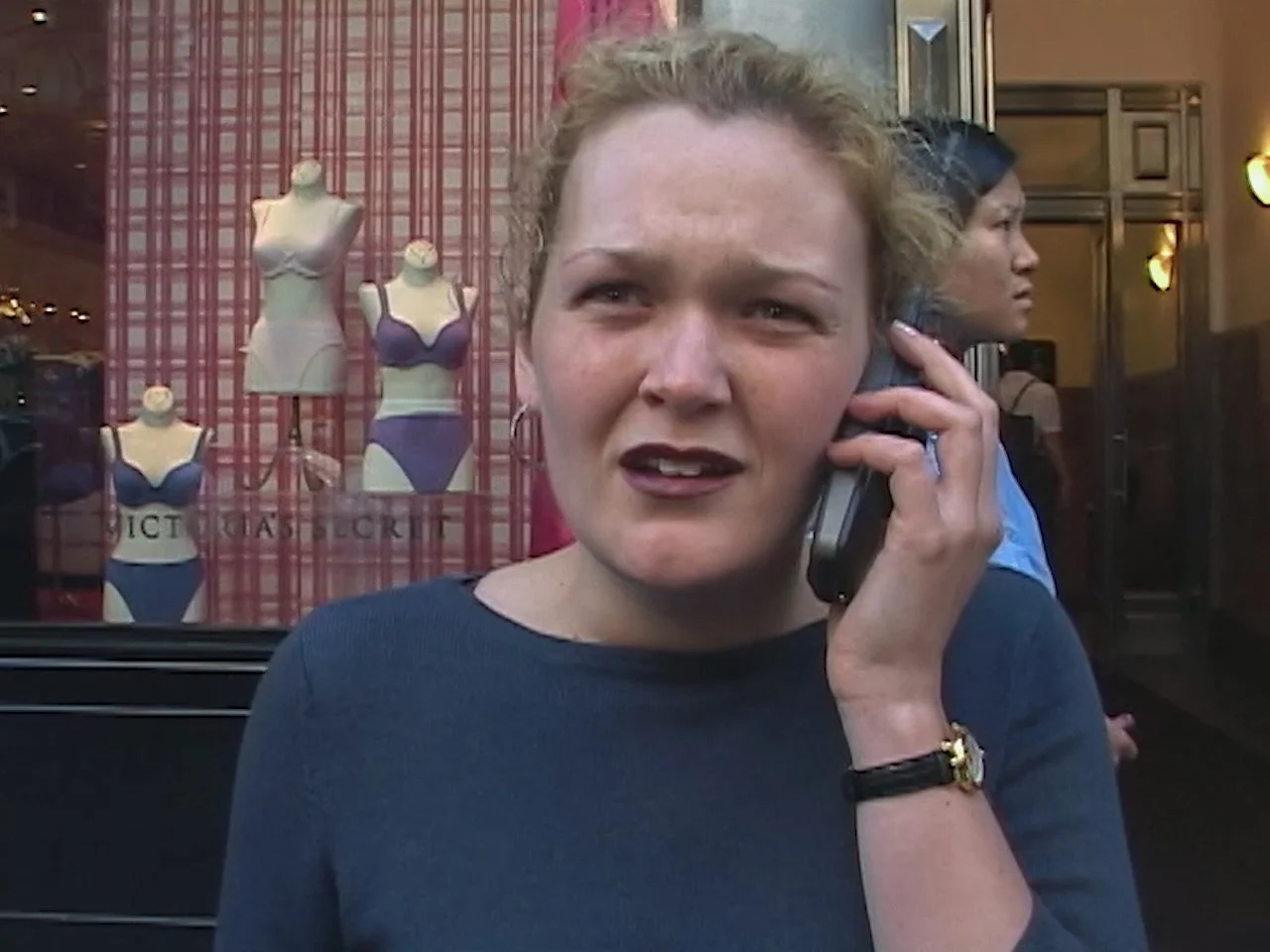 A woman with curly hair and a worried expression talking on a cell phone on. 5th Avenue New York City.   9/11 September 11th 2001
