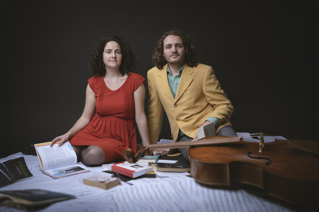 Portrait du duo Camille Claudel composé de Noémie Berz et Kevin Bourdat, entourés de livres, de partitions et d'un violoncelle.