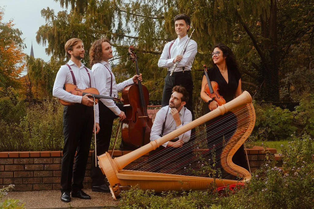 Portrait du Quintette Le Bateau Ivre composé de Samuel Casale à la flûte, Séréna Manganas au violon, Valentin Chiapello à l'alto, Kevin Bourdat au violoncelle et Jean-Baptiste Haye à la harpe, en extérieur dans un cadre champêtre.