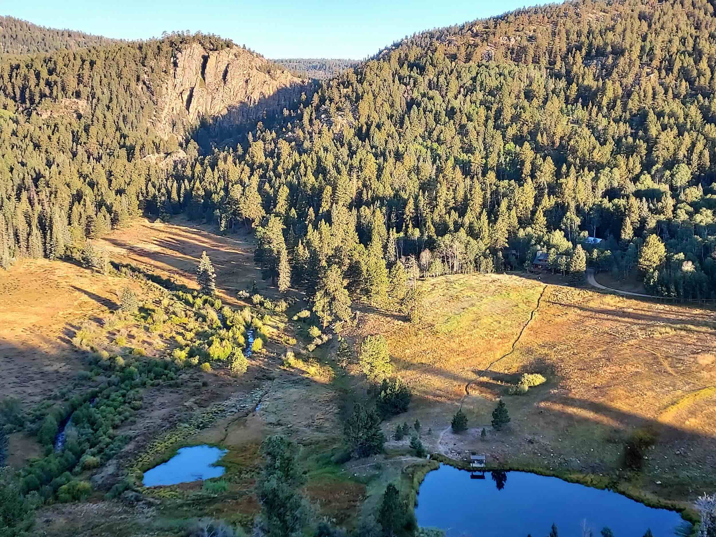 A mountainous landscape at Vallecito with dense evergreen trees covering the hillsides, a small winding river in the valley, and a few buildings.