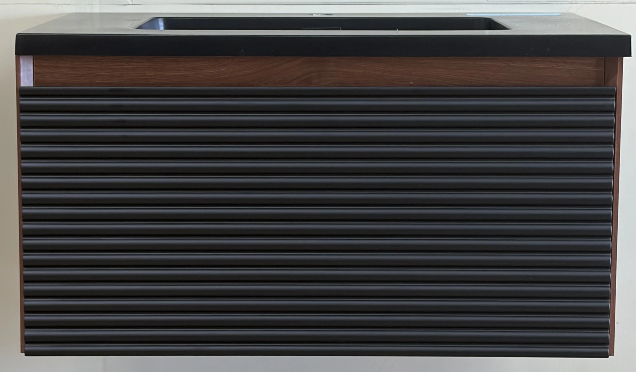 A modern black and brown kitchen island with horizontal black metal slats on the front, a black countertop, and a built-in sink.