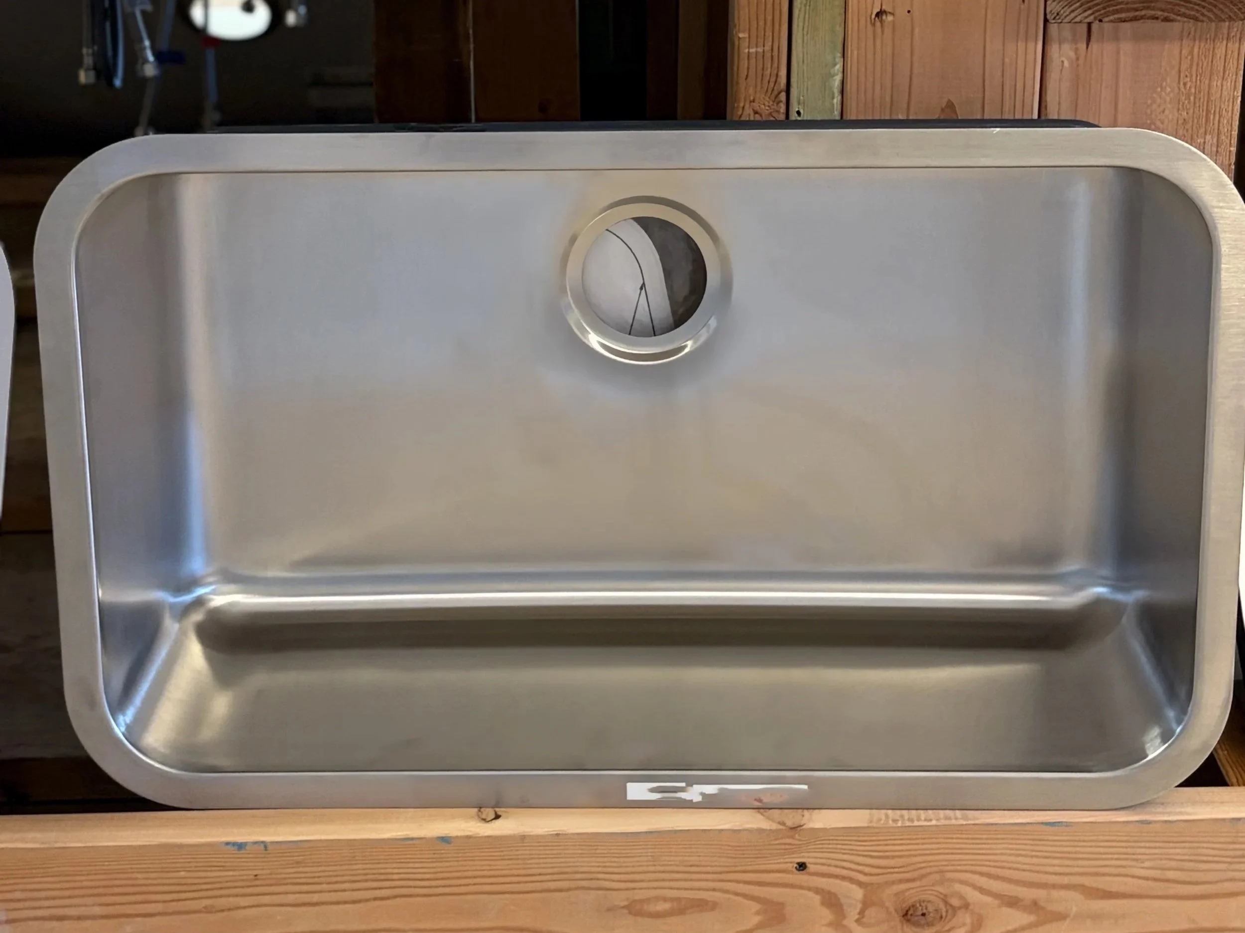 A stainless steel sink with a single basin, mounted on a wooden countertop in a rustic setting.