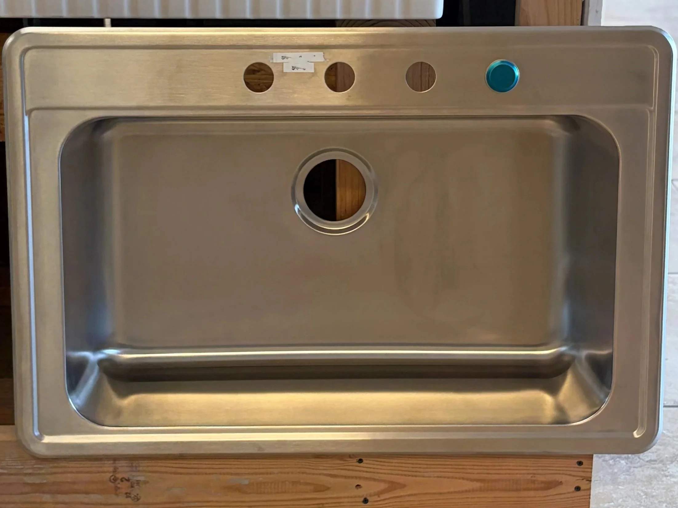 Stainless steel kitchen sink with cutout for a faucet and holes for accessories, mounted on a wooden countertop.