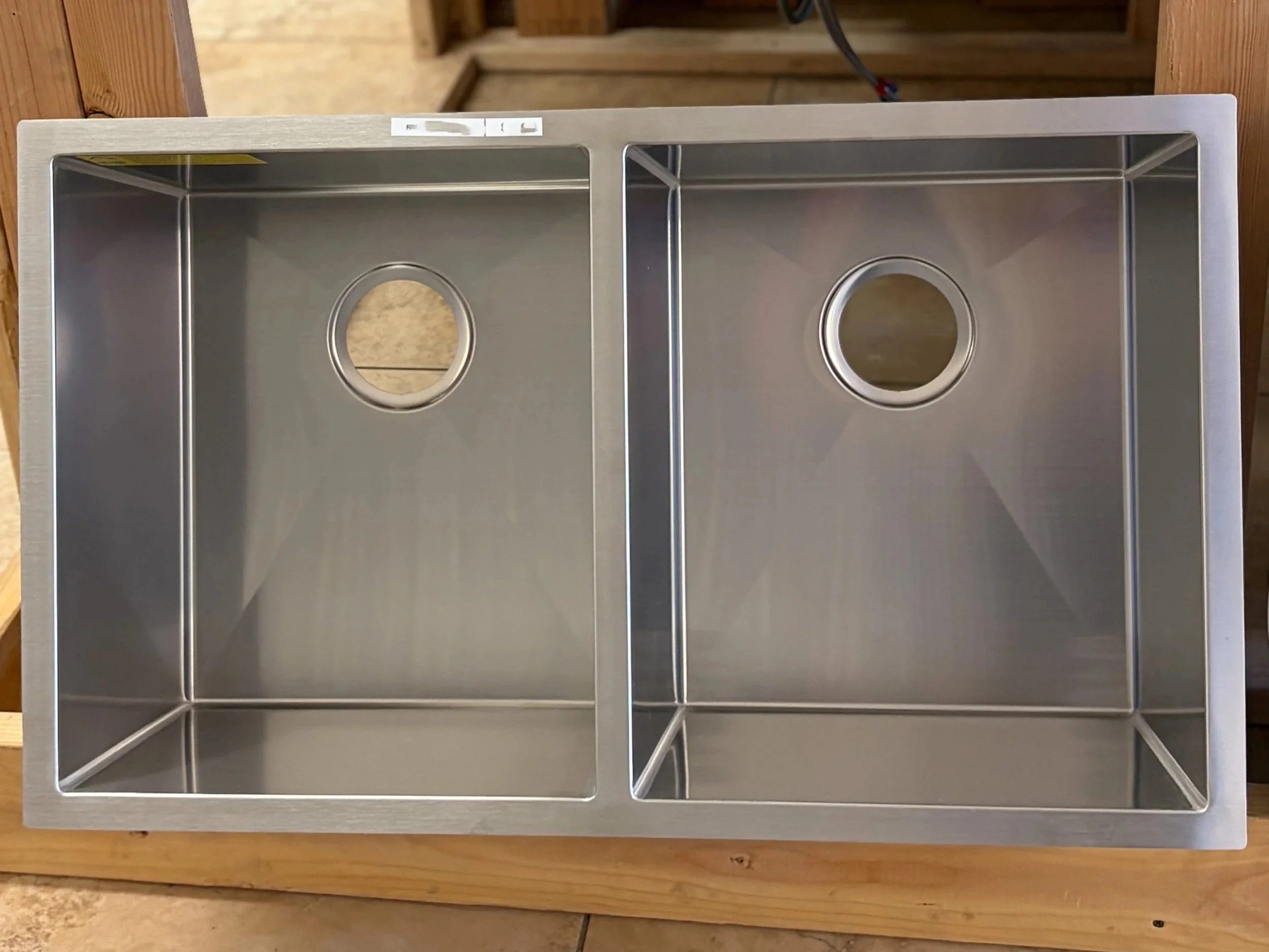 A stainless steel double-basin kitchen sink with circular drain openings, mounted on a wooden countertop.