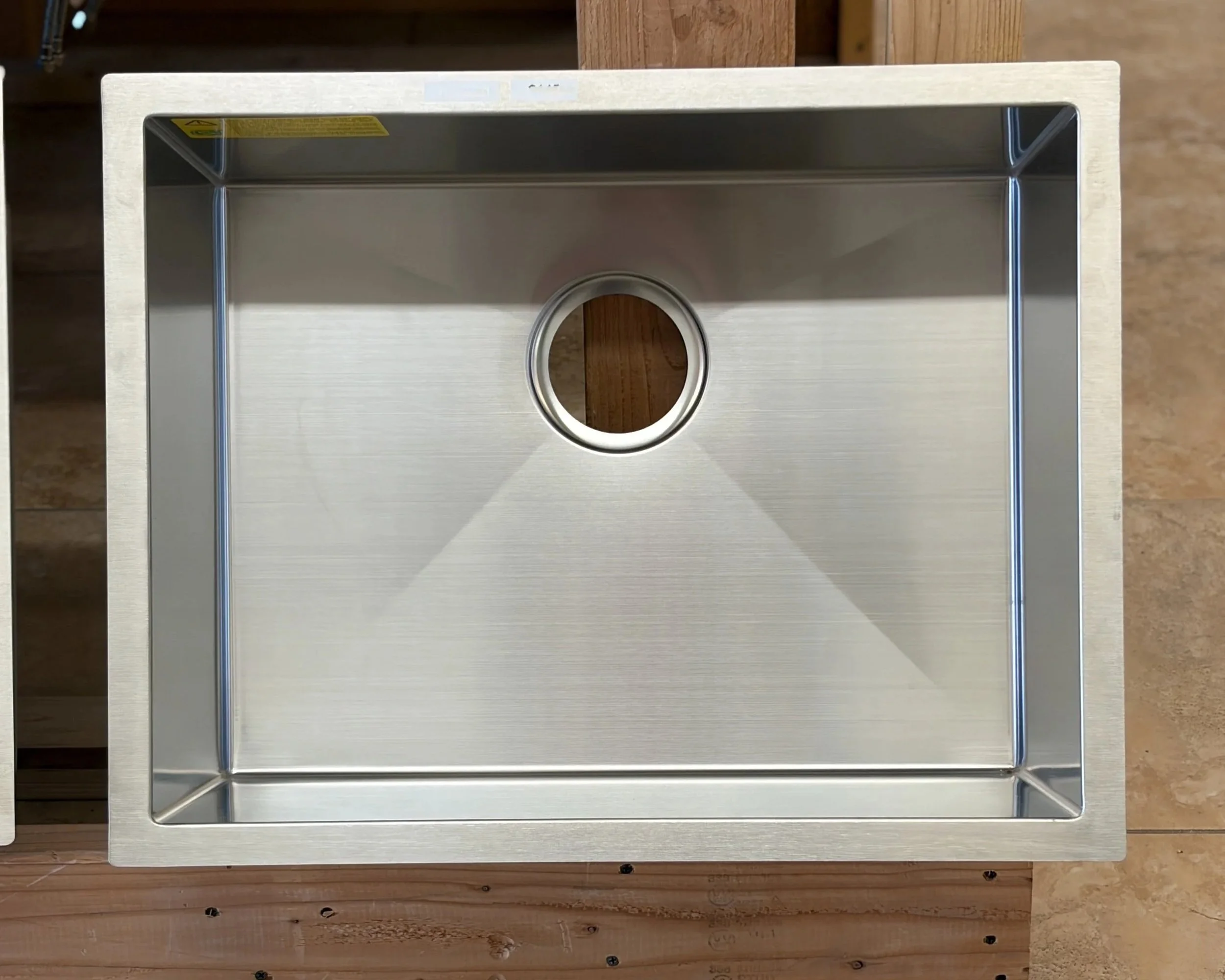 Top view of a stainless steel box or container with a circular hole in the center, placed on a wooden surface.