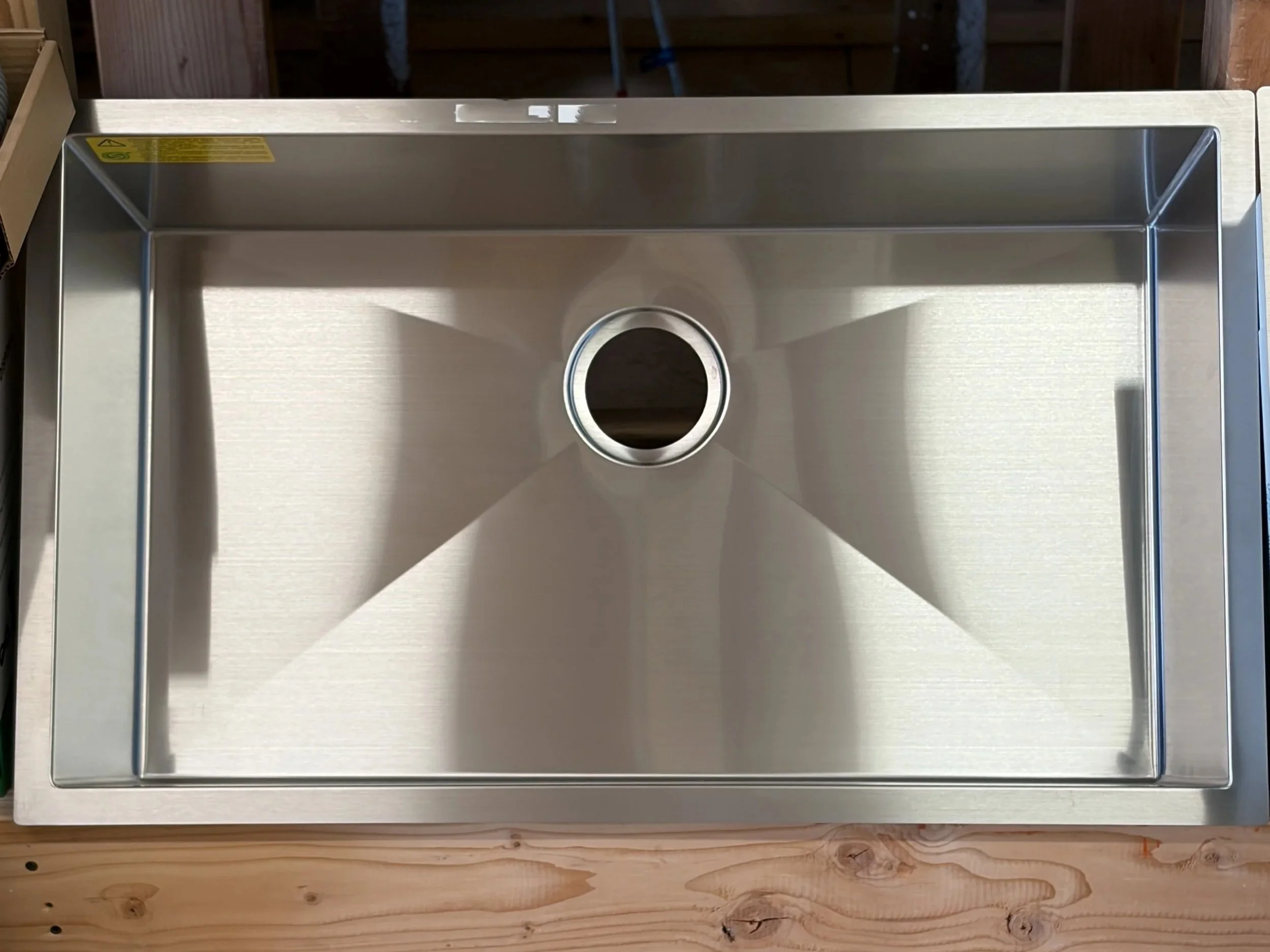 A stainless steel kitchen sink with a circular drain in the center, installed in a wooden countertop with visible wood grain and knots.