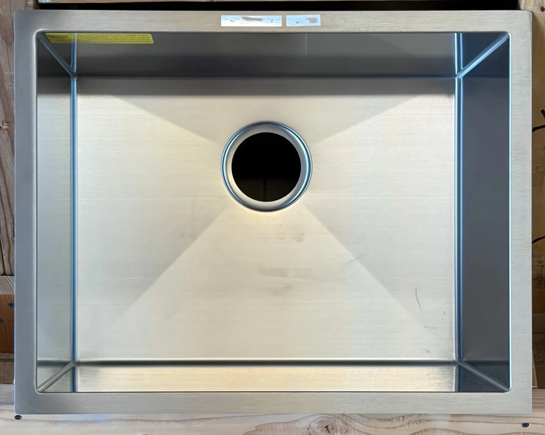 Top view of a stainless steel frame with a circular hole in the center, placed on a wooden surface.
