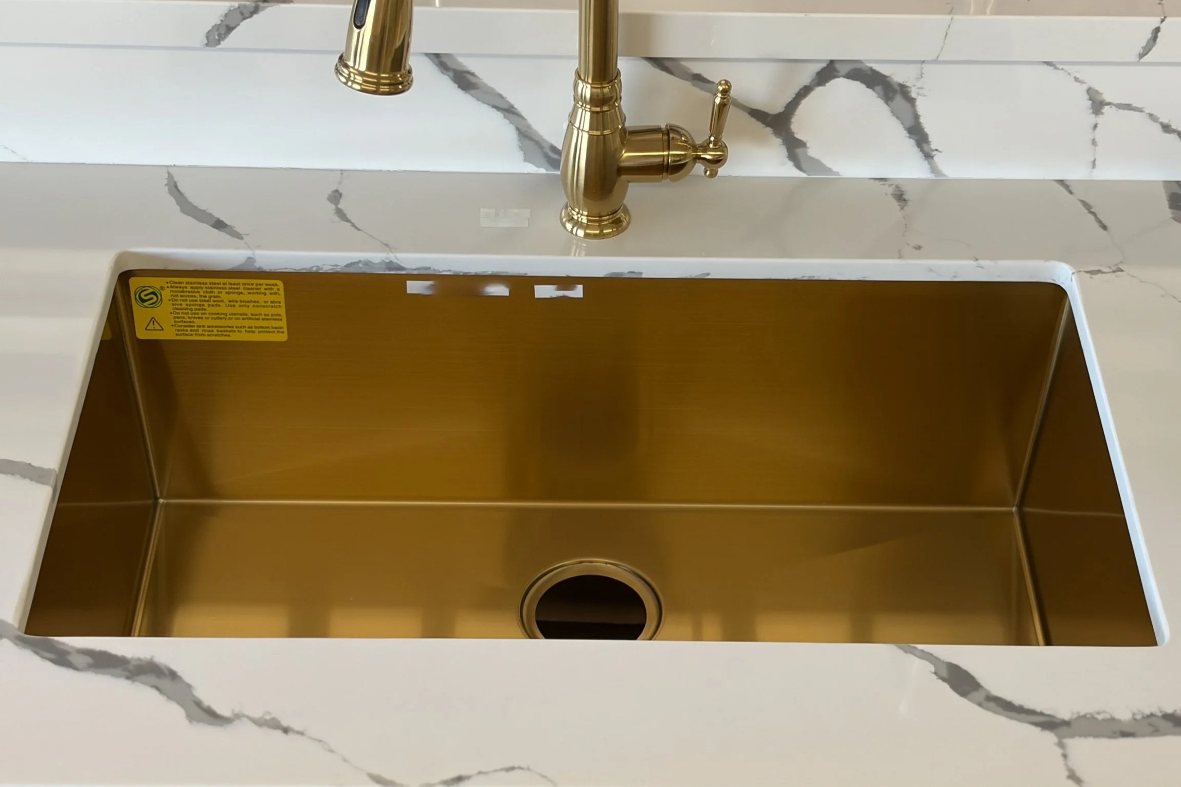 A kitchen sink with a golden faucet and a white and gray marble countertop.
