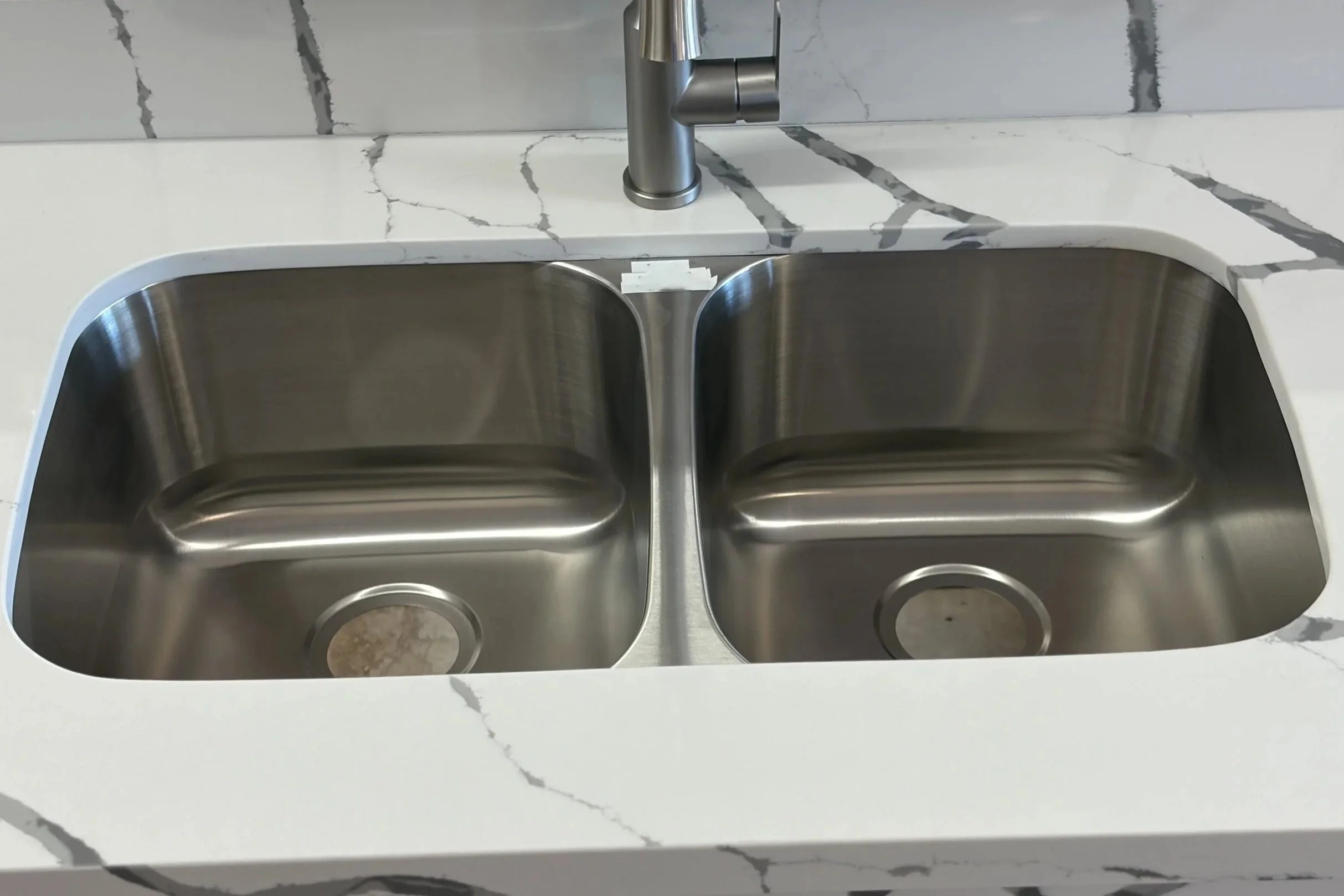 Double stainless steel kitchen sink installed in white marble countertop with gray veining.
