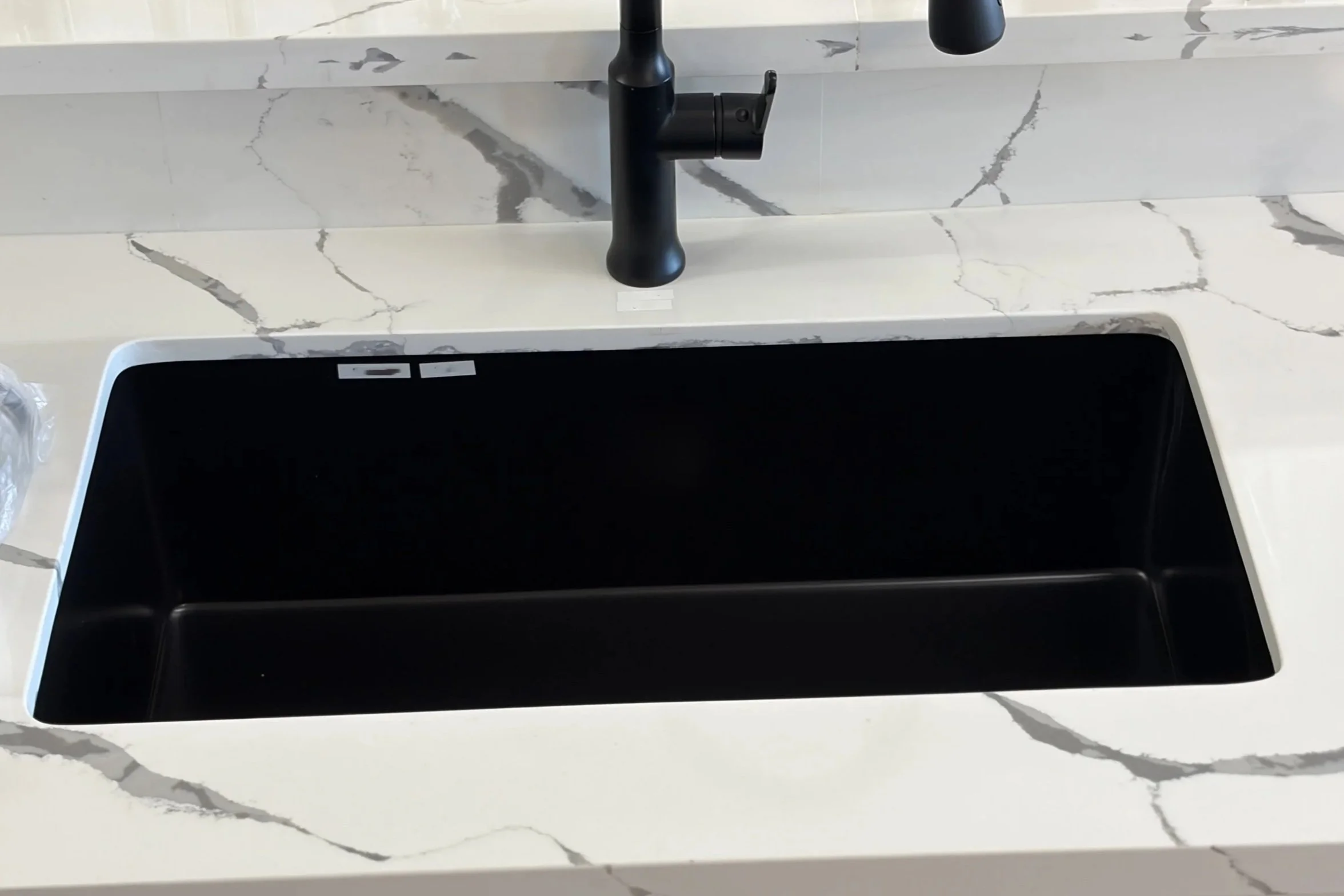 View of a kitchen countertop with a marble pattern, a black sink, and a black faucet.