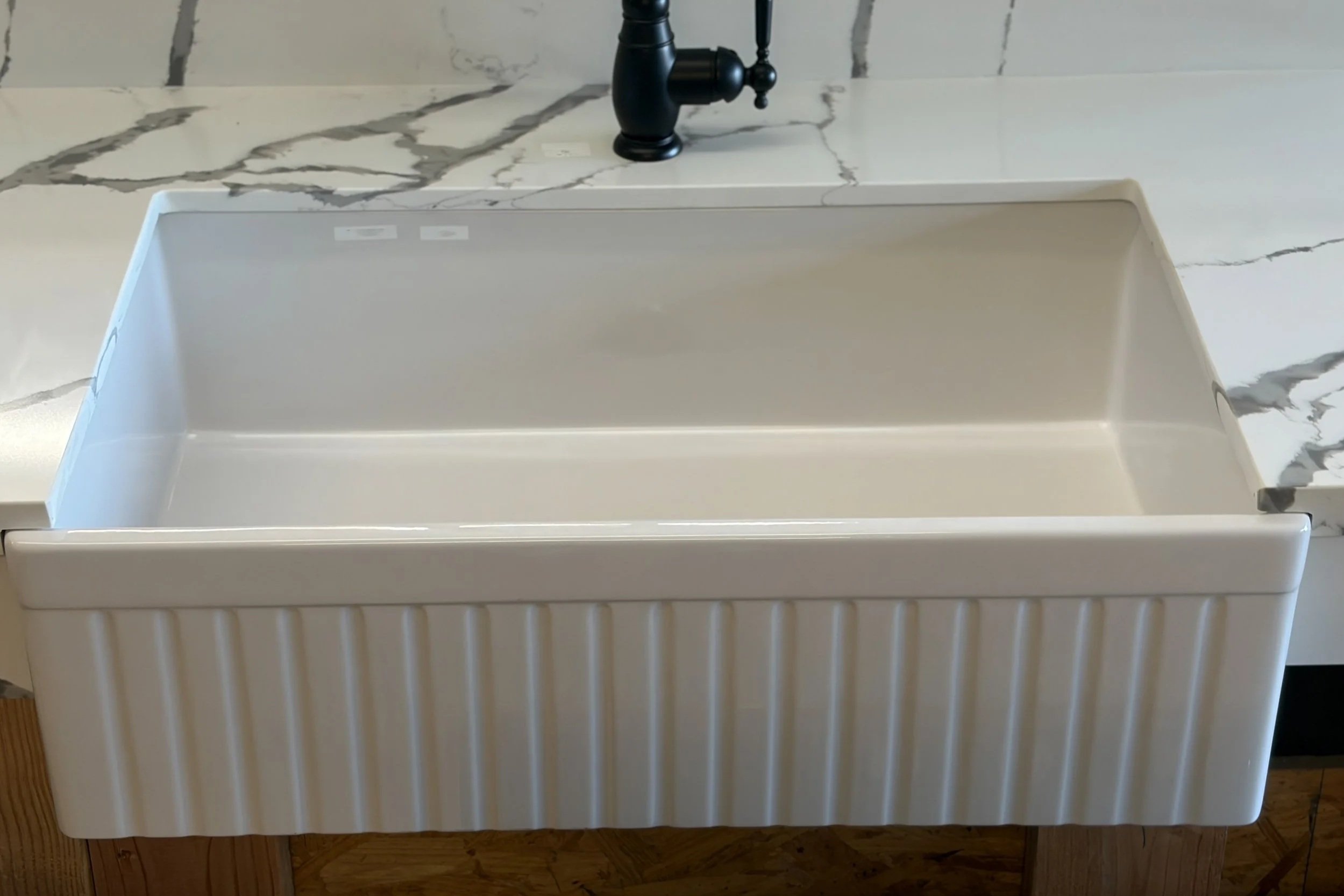 A kitchen sink with a black faucet and a marble-patterned backsplash. The sink appears to be a step or drying rack style with a slatted front.