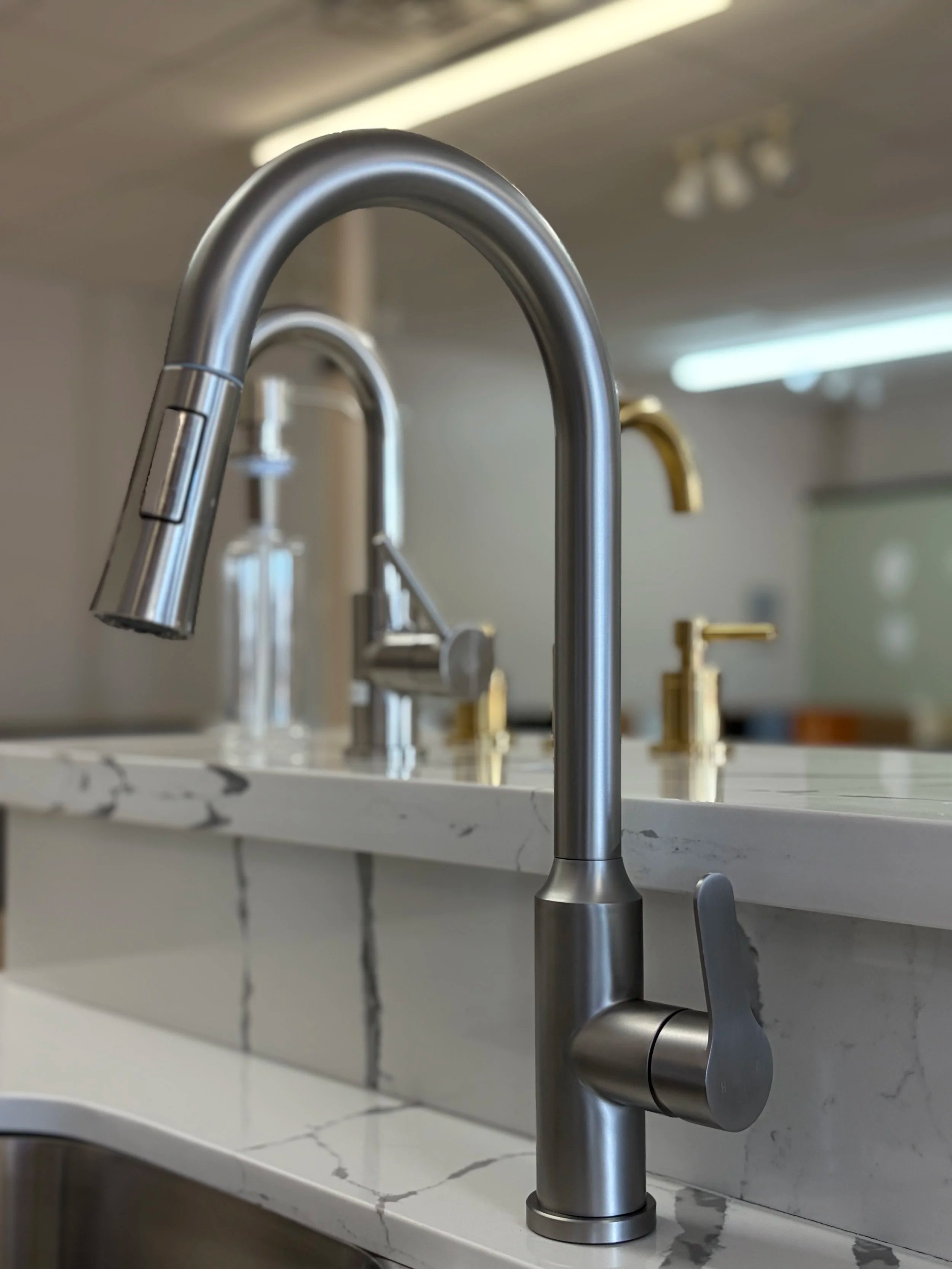 Close-up of a modern kitchen faucet with a curved spout and a single handle, installed on a white marble countertop.
