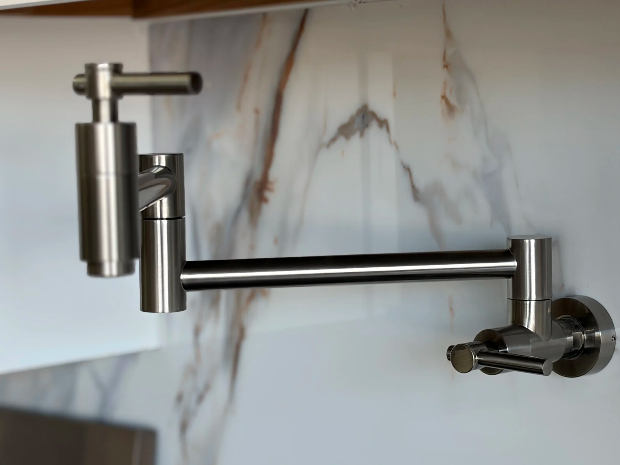 Close-up of a modern stainless steel kitchen faucet mounted on a white marble countertop with brown veining.