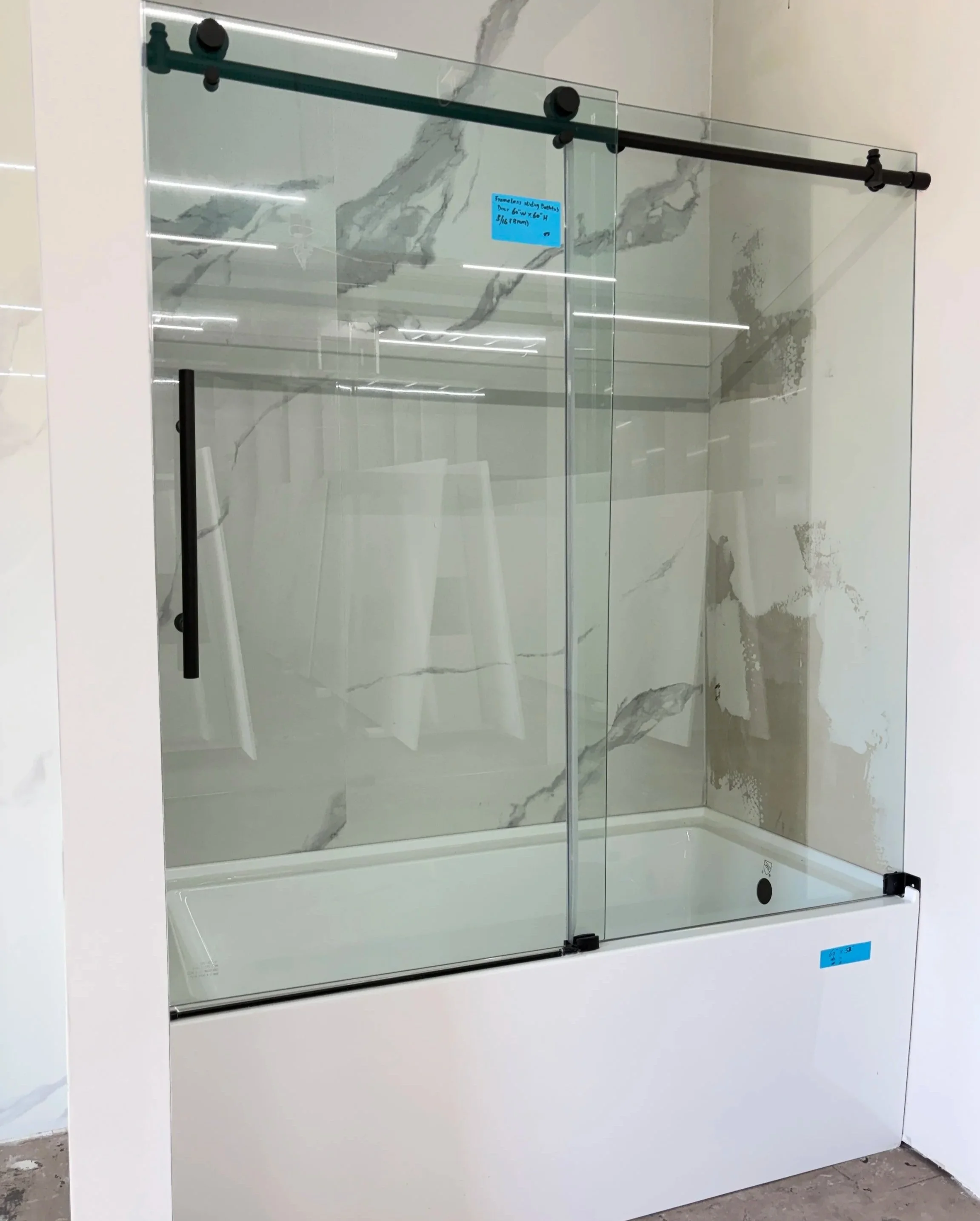 A glass shower enclosure with black hardware and marble-patterned wall tiles inside a bathroom.