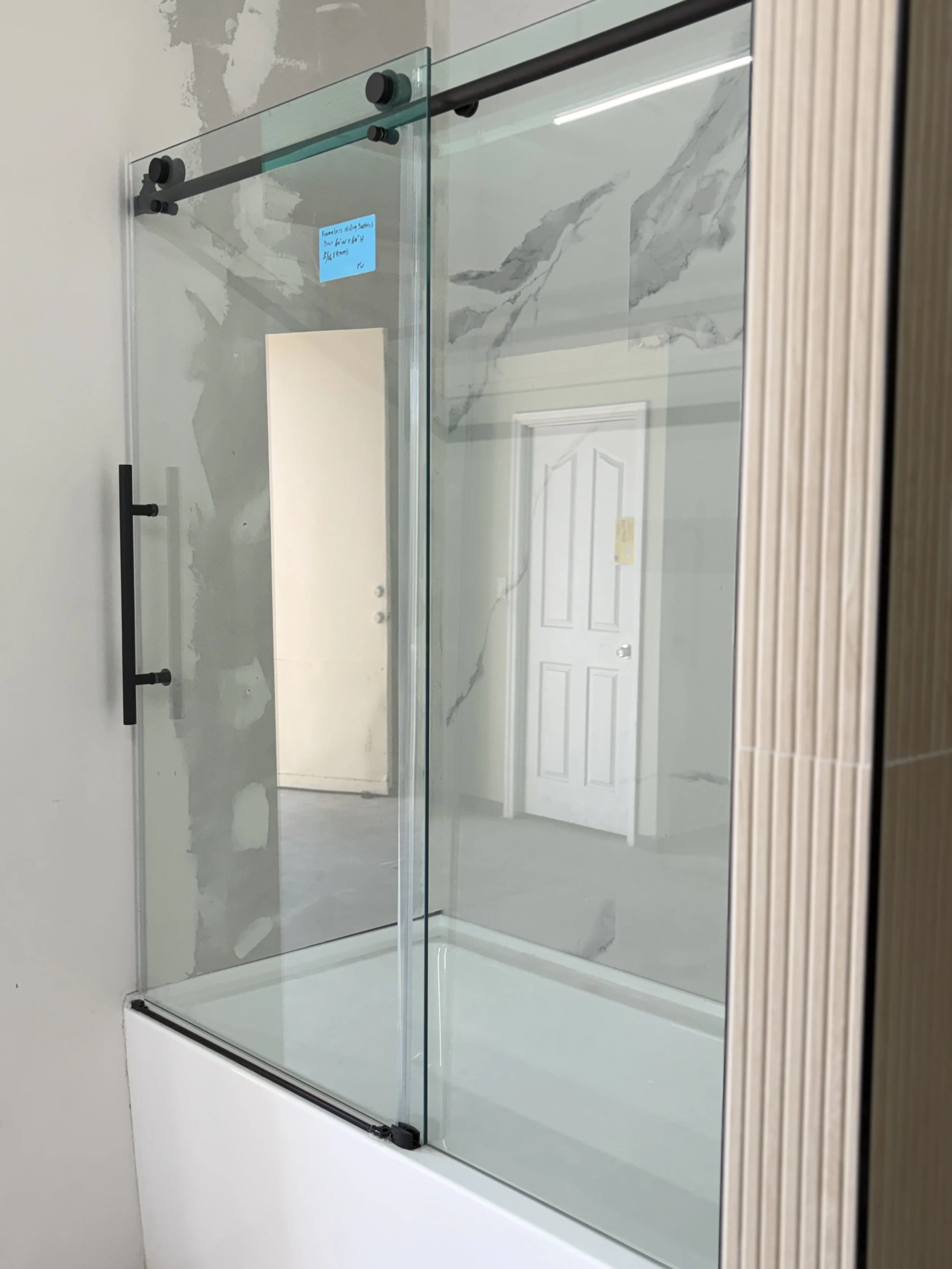 A glass shower enclosure with black hardware and a marble wall in the background.