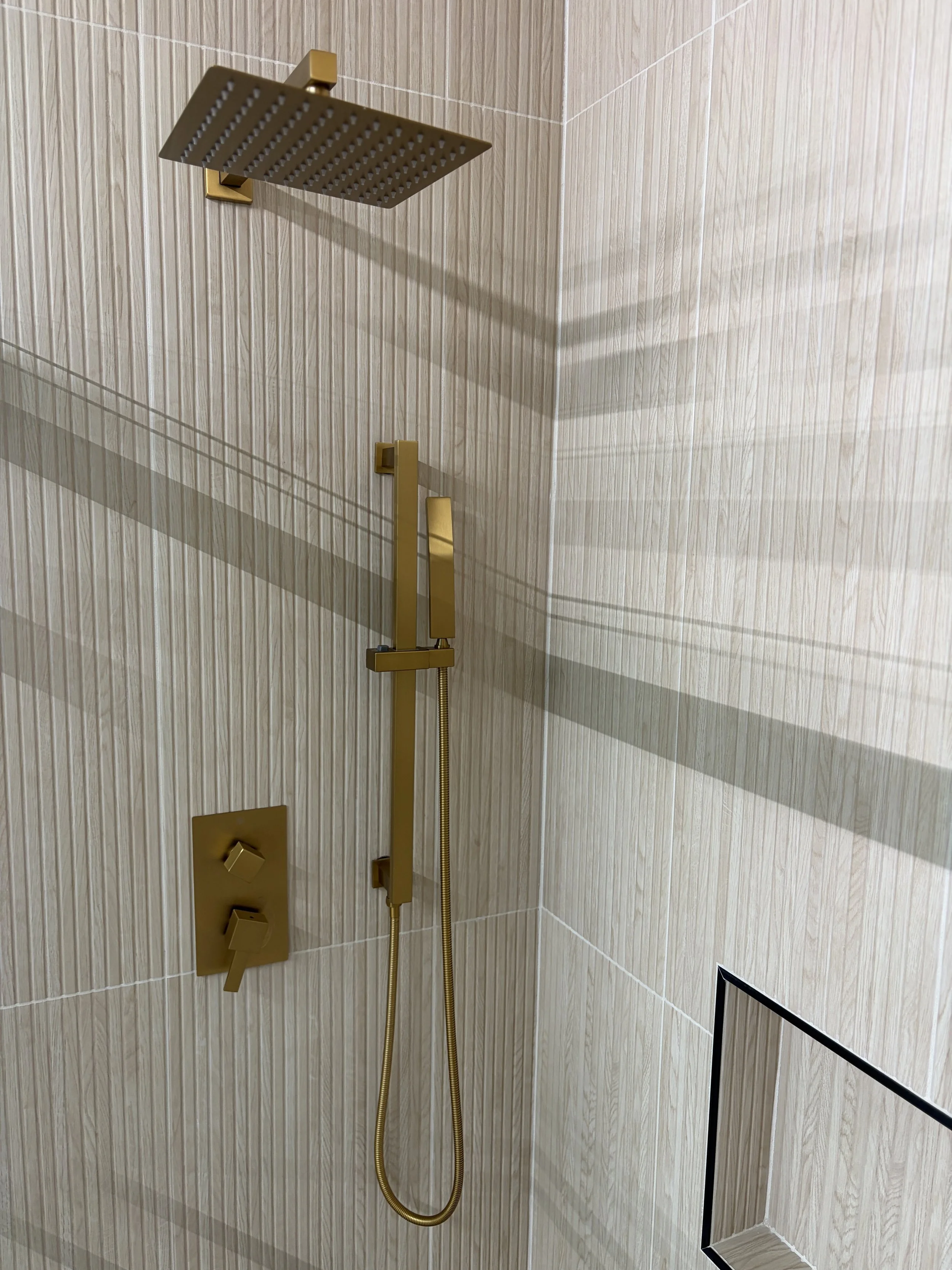 A modern shower with a large square showerhead, golden fixtures, and a beige tiled wall.