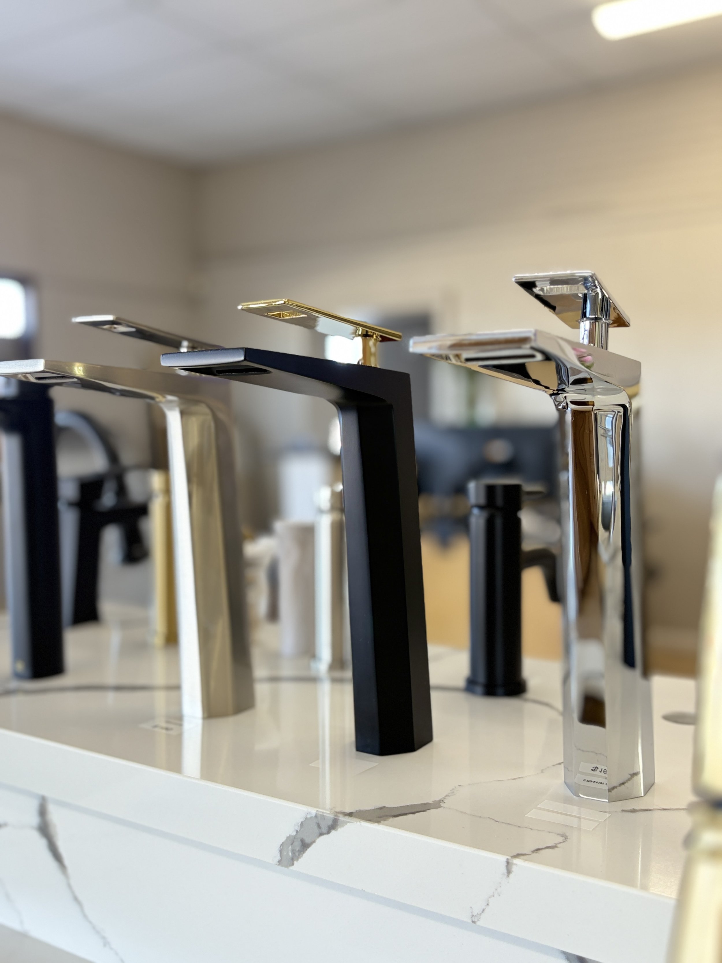 Collection of modern kitchen faucet taps in black, gold, silver, and marble on a white marble countertop.