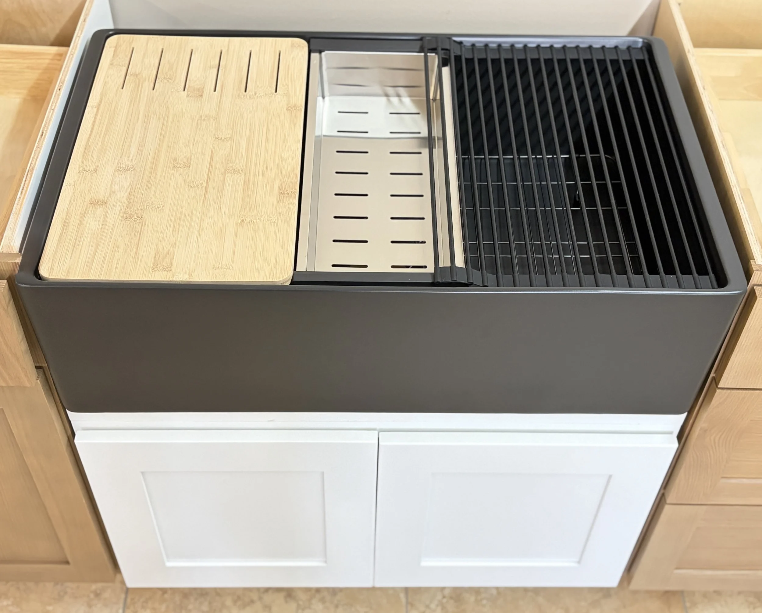 A kitchen countertop with a wooden cutting board on the left, a metallic slotted insert in the middle, and a black grill on the right, surrounding a black frame.