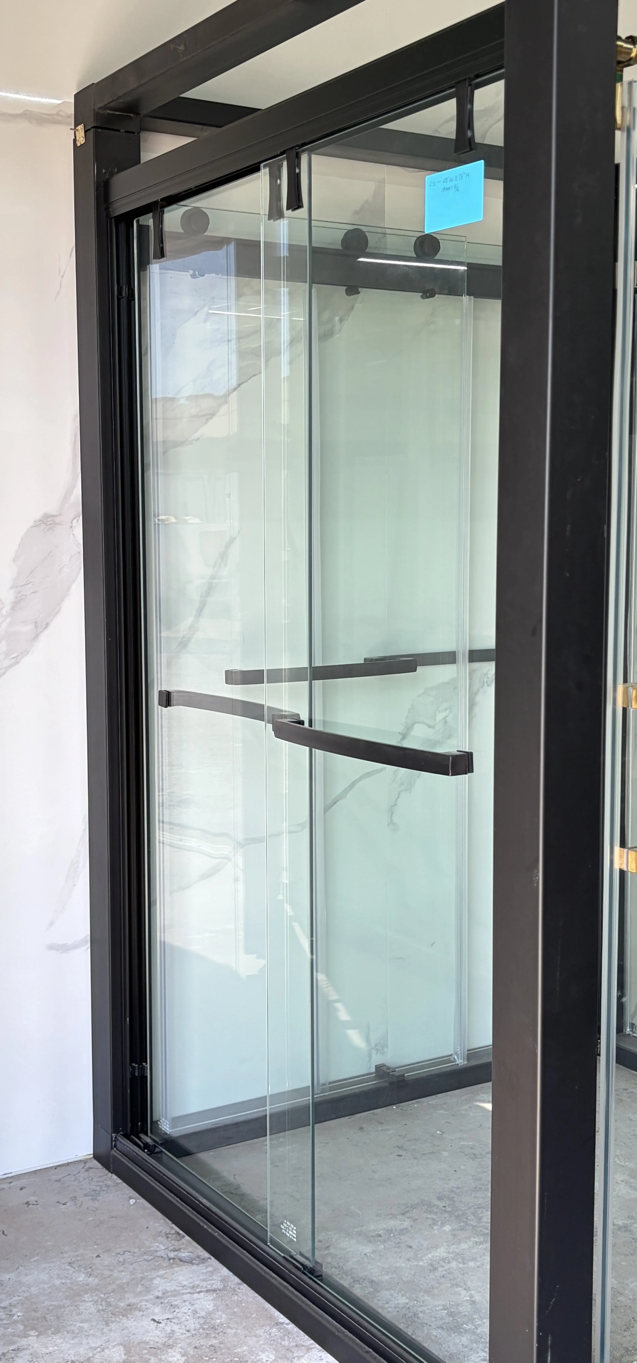 A glass shower enclosure with black metal framing and black handles, located in a modern bathroom with marble walls and concrete floor.