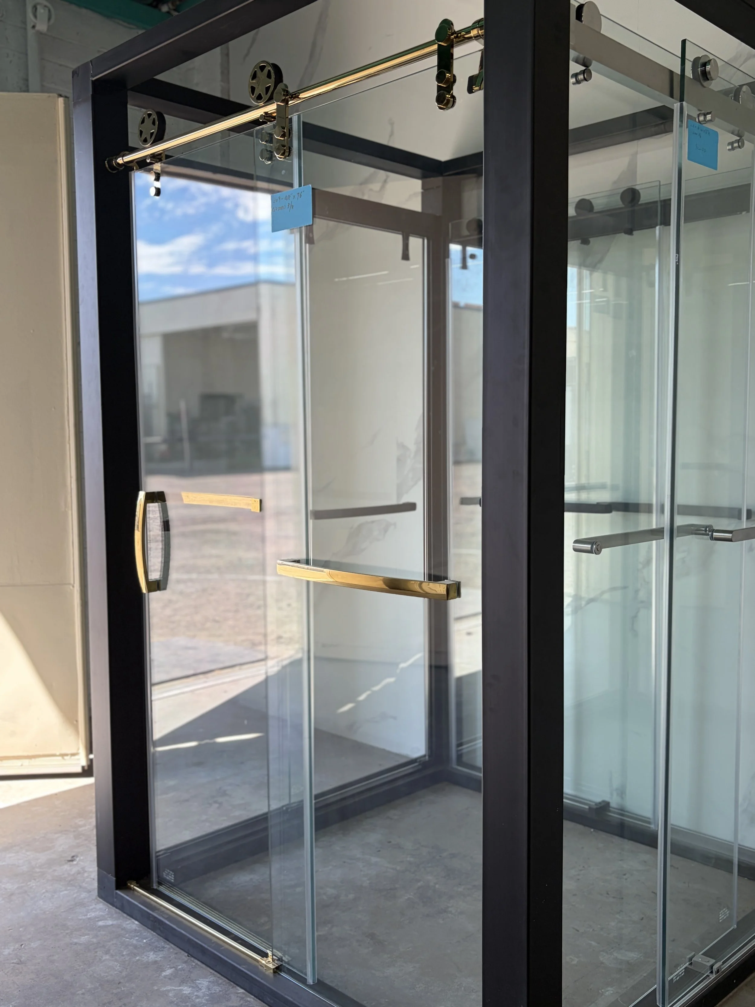 Empty glass display case with gold accents, set in a modern interior or showroom, with a reflection of a blue sky with clouds visible in the glass.