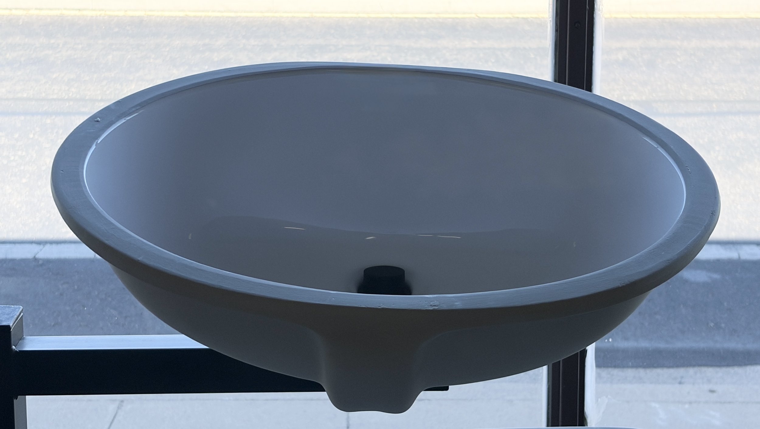 White porcelain sink with a black drain in the center, positioned outdoors near a window with a metal frame.