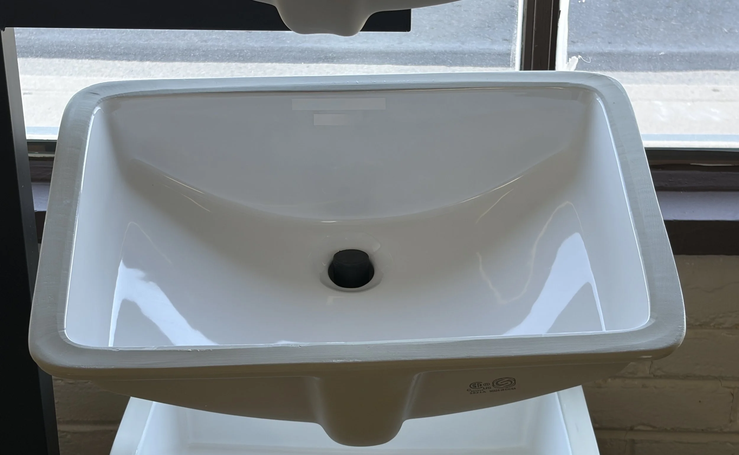 A white feet washing basin with a black soap dispenser in the center, placed on a white stand.