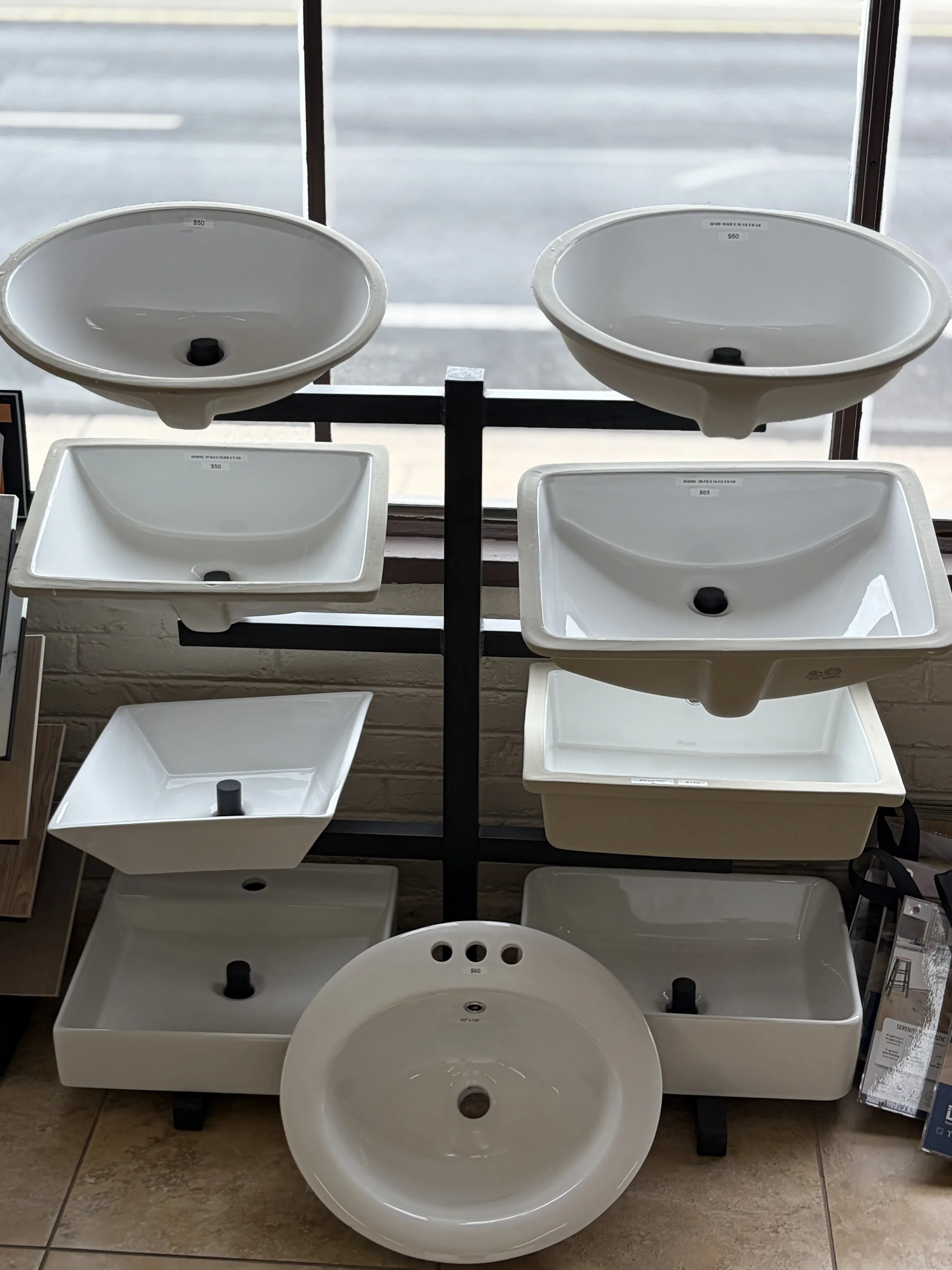 Display of white bathroom sinks in a store with a window in the background.