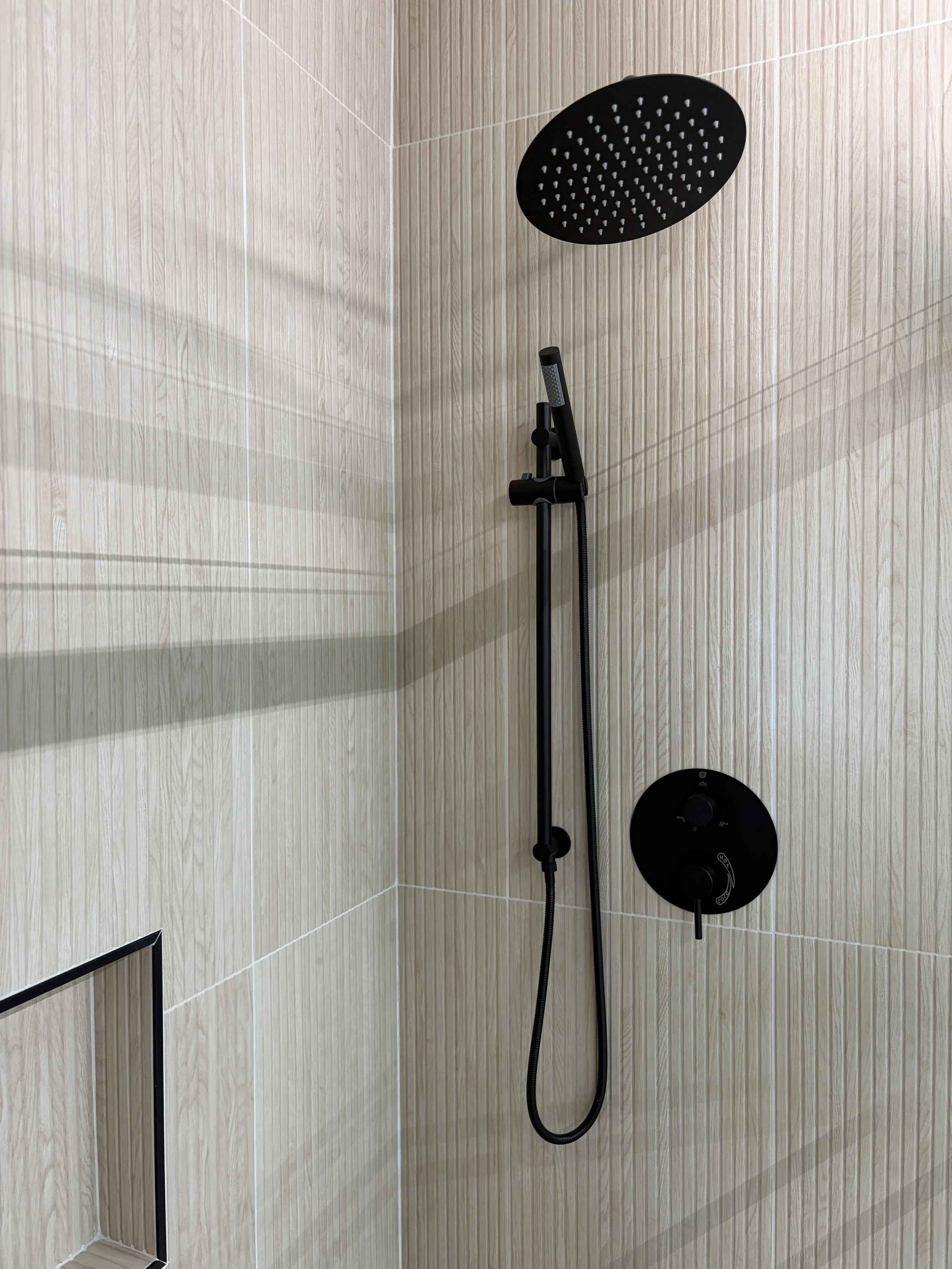 Shower with black rainfall showerhead and hand-held showerhead mounted on beige tiled wall.