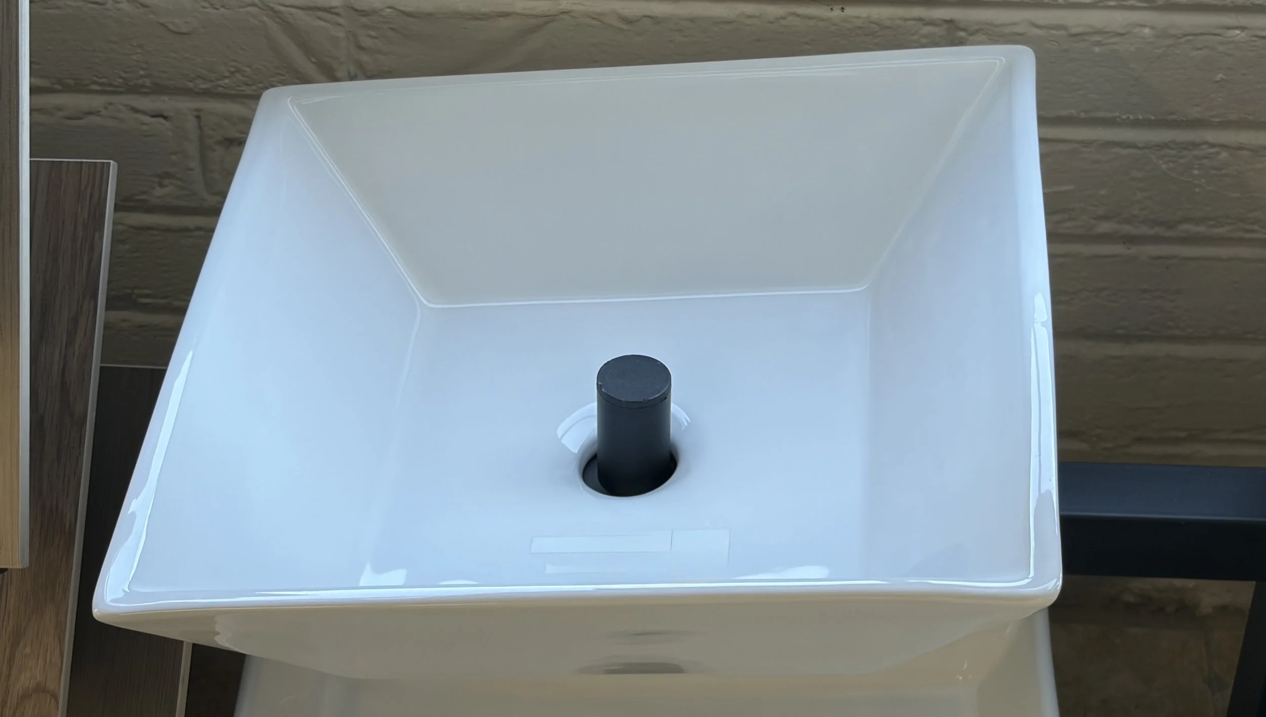 Top view of a white atomizer with a black nozzle, placed inside a square container, with wood panels visible on the side.