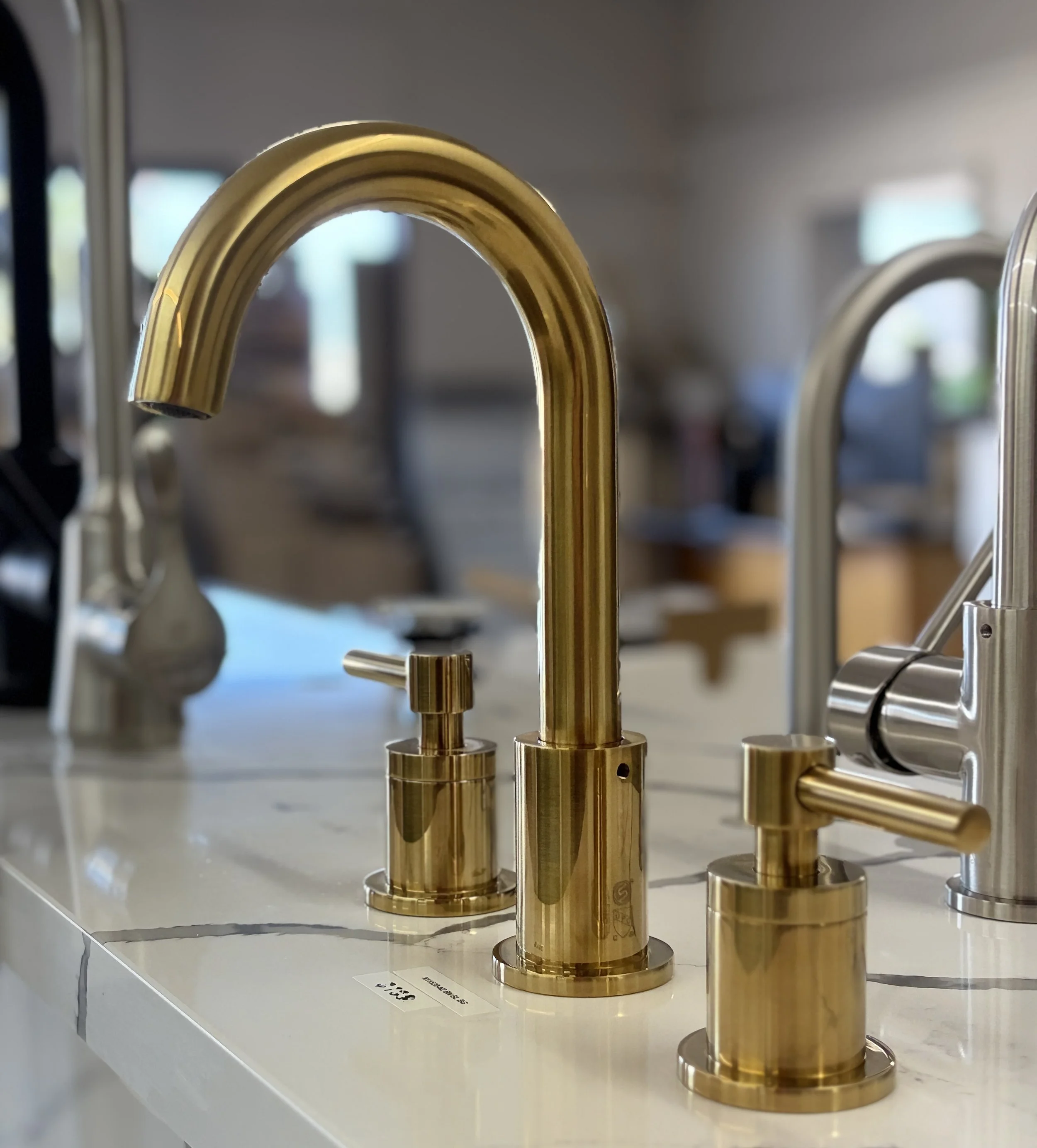 Close-up of a shiny gold kitchen faucet on display at a store, with other faucets visible in the background.