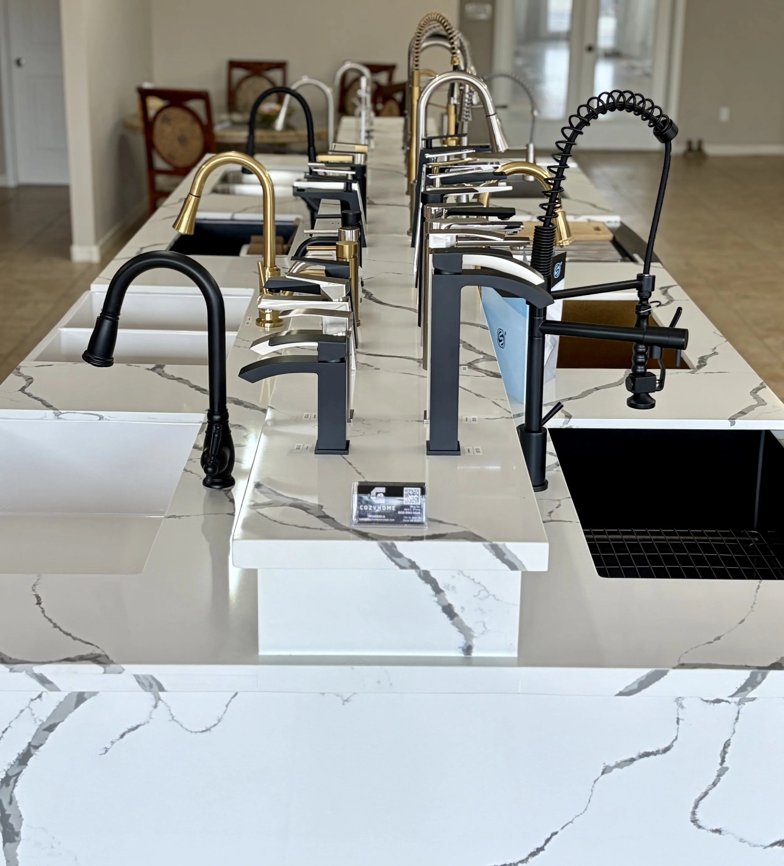 Display of various kitchen faucets and fixtures on a marble countertop in a showroom.
