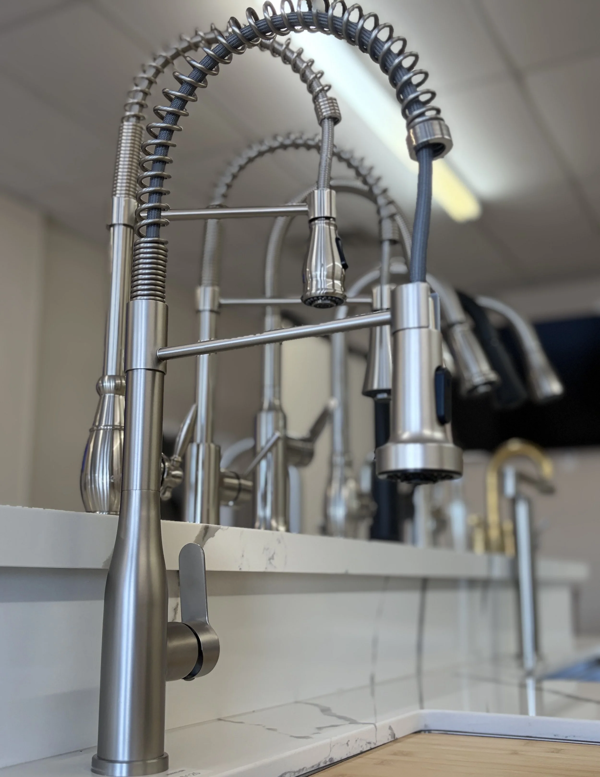 Multiple stainless steel kitchen faucets mounted on a white marble countertop with a marble backsplash in a modern kitchen.