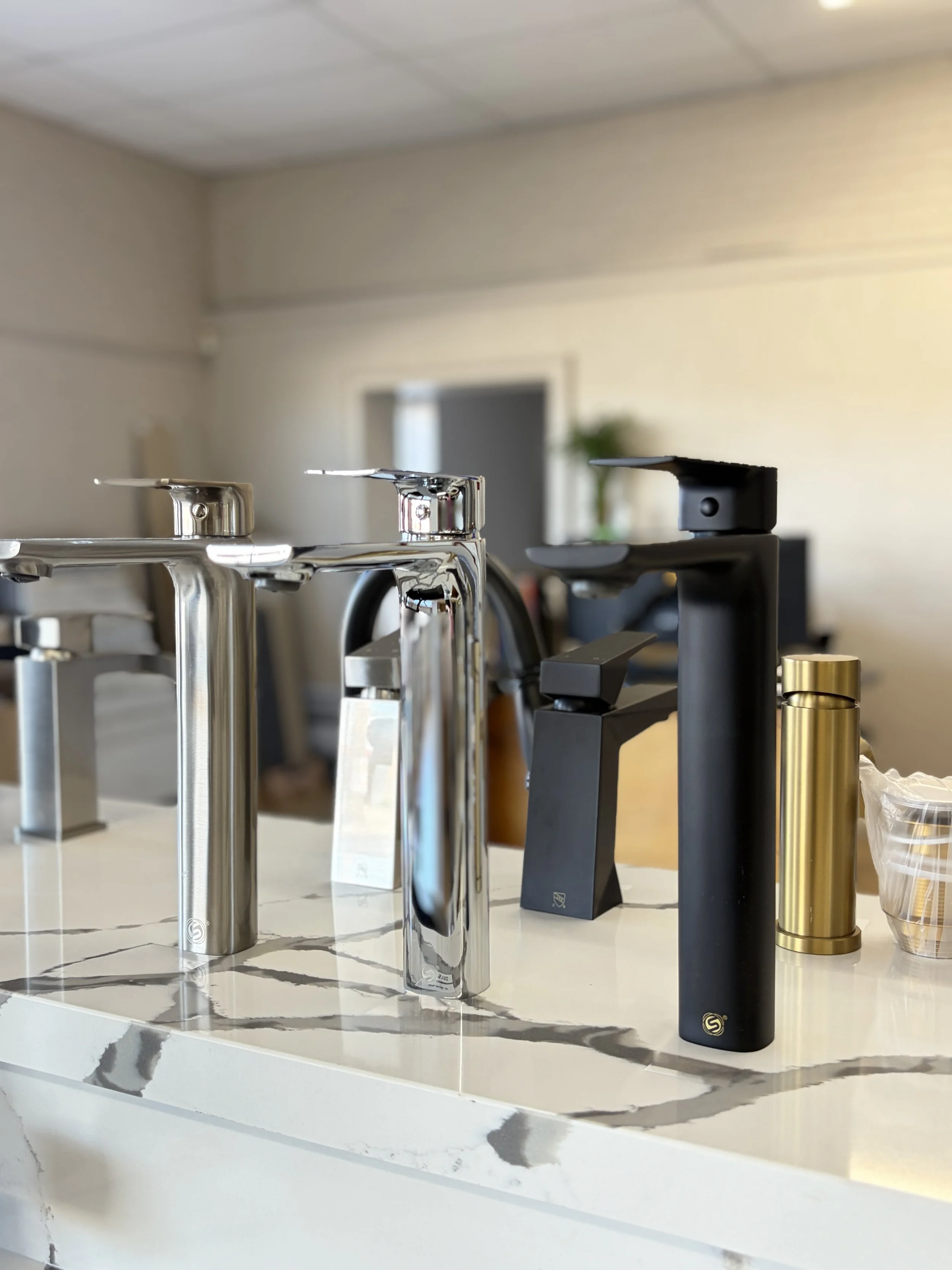 A display of various modern kitchen faucets and spray dispensers on a marble countertop.