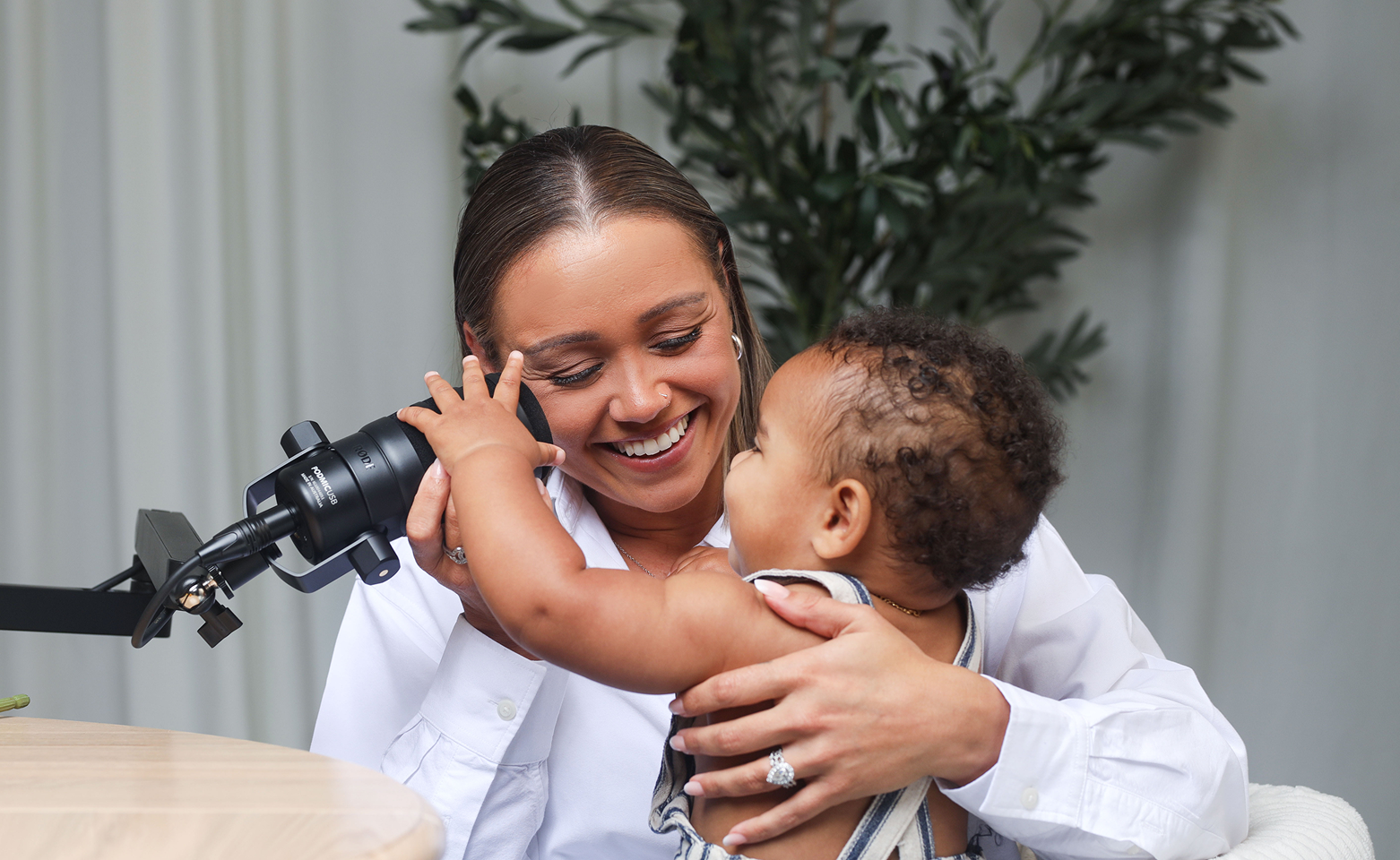 A woman and a young child play together with a microscope in a bright room with a plant in the background.