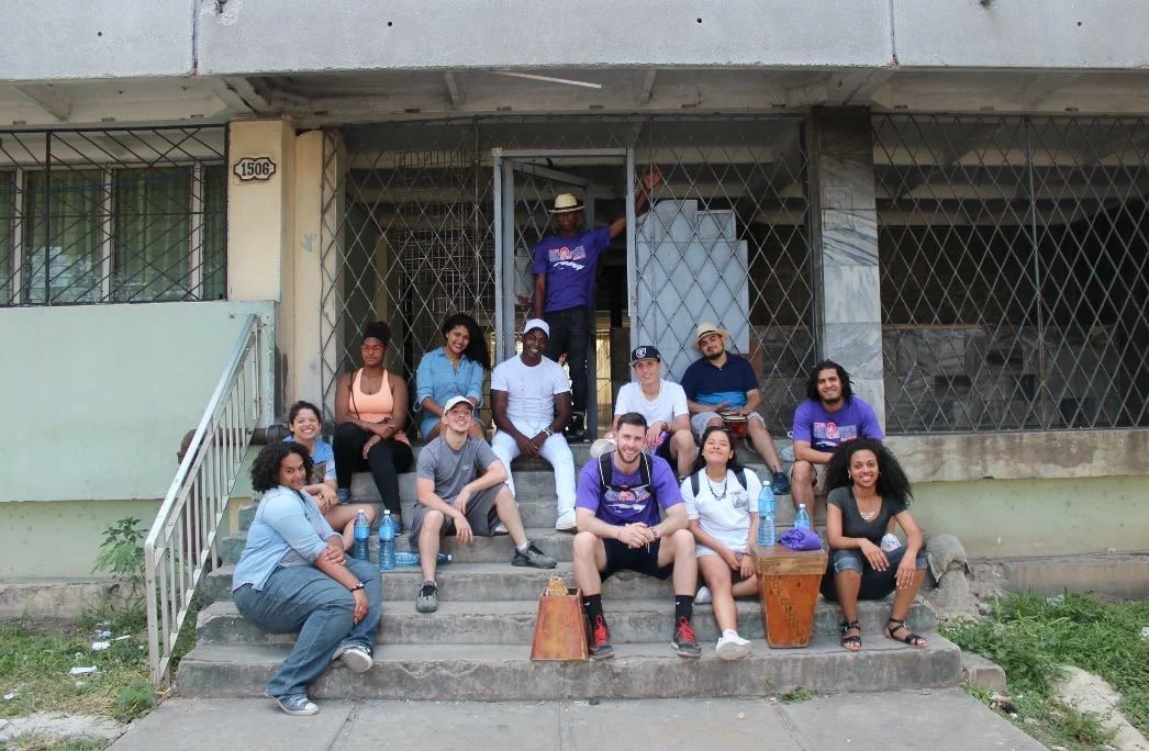 Group of people sitting and standing on the steps of a building, posing for a photo.
