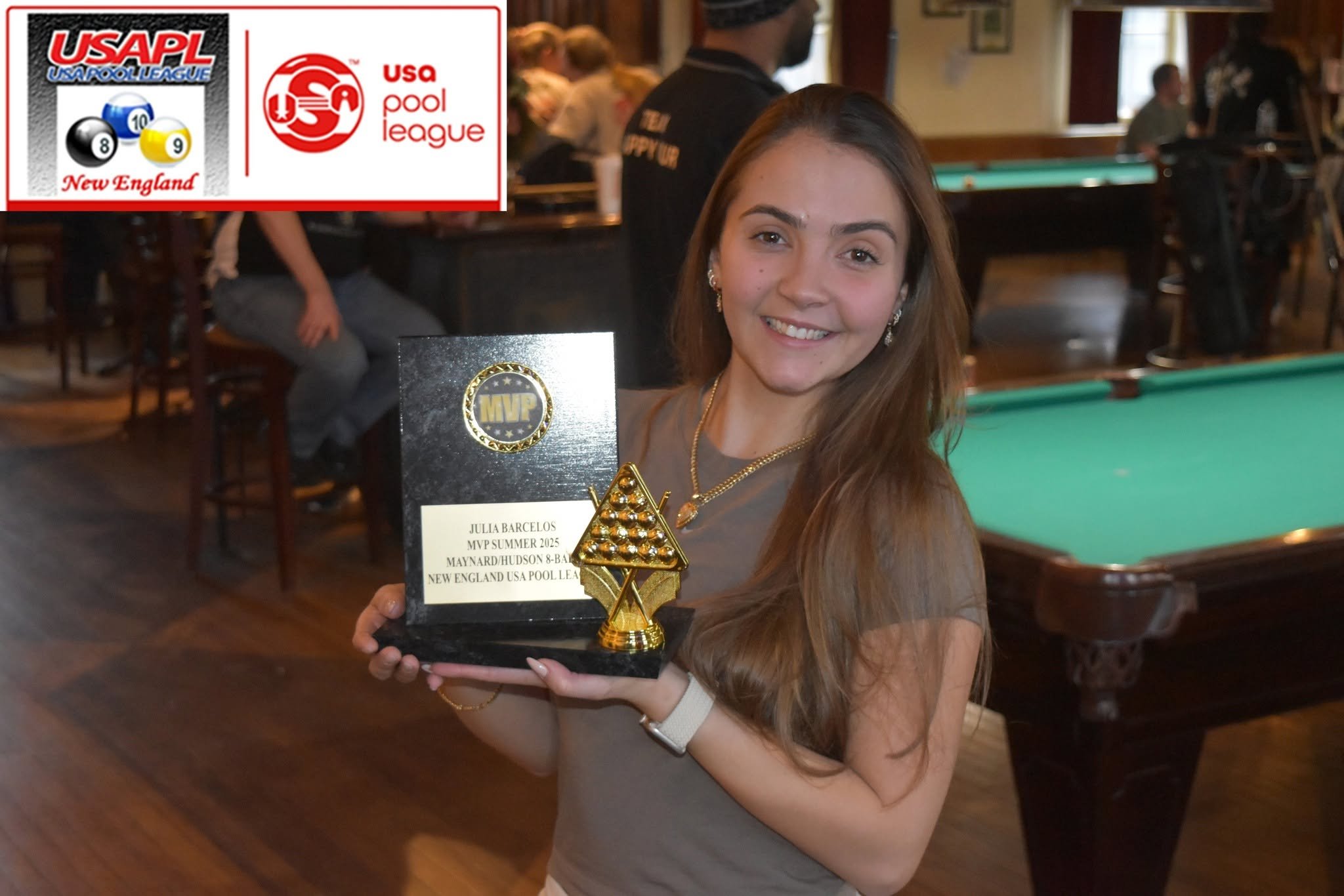 Young woman with long red hair smiling and holding a plaque and trophy in a pool hall, with pool tables and other people in the background. The plaque reads 'Julia Barcelos, MVP Summer 2023, Maynard/Hudson 8-Ball, New England USA Pool League'.