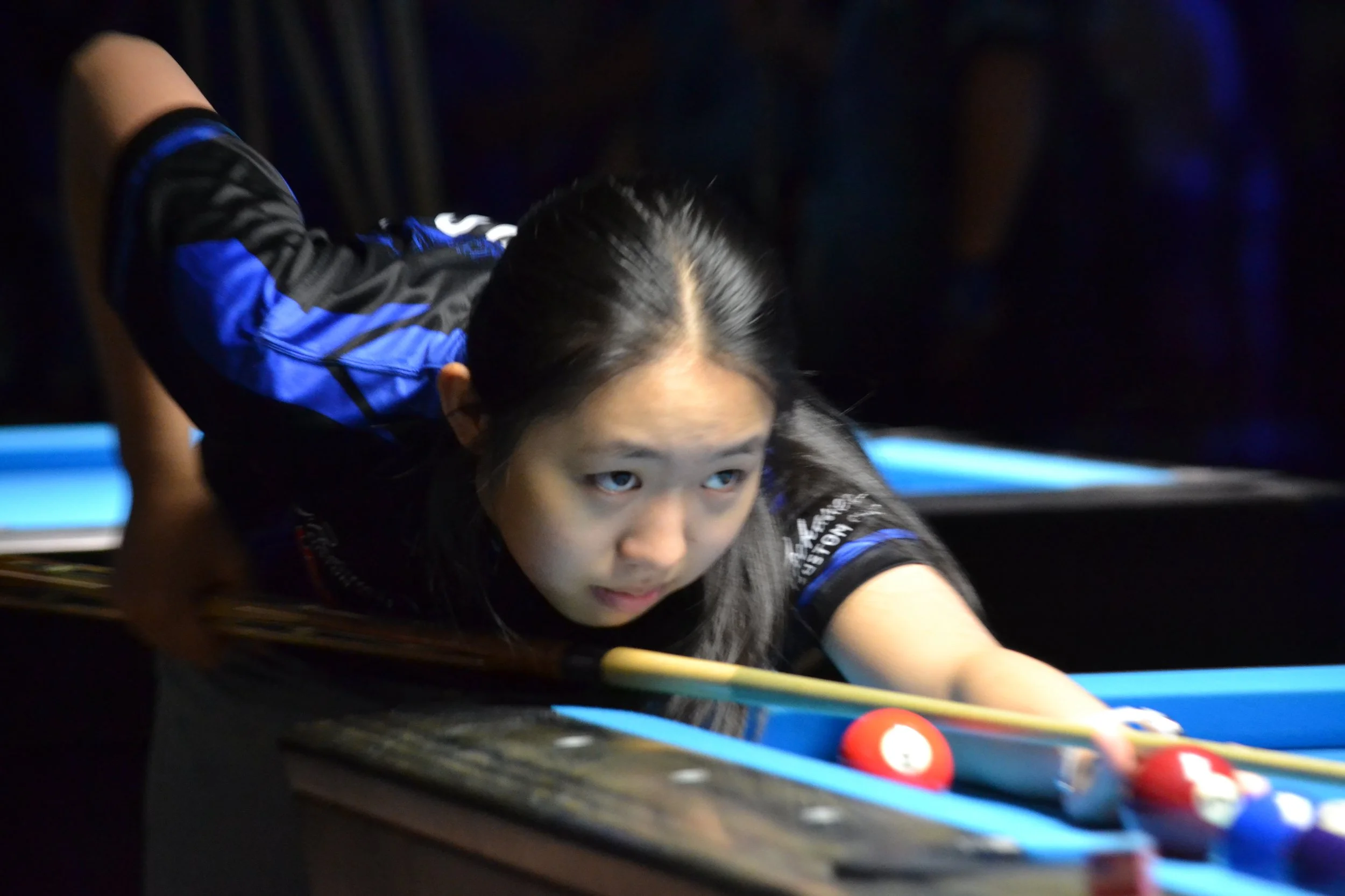 A person playing billiards or pool, leaning over a pool table aiming to hit the balls.