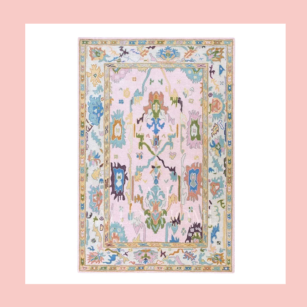 Colorful patterned area rug with pastel pink, blue, green, purple, and yellow shapes and borders, on a pink background.