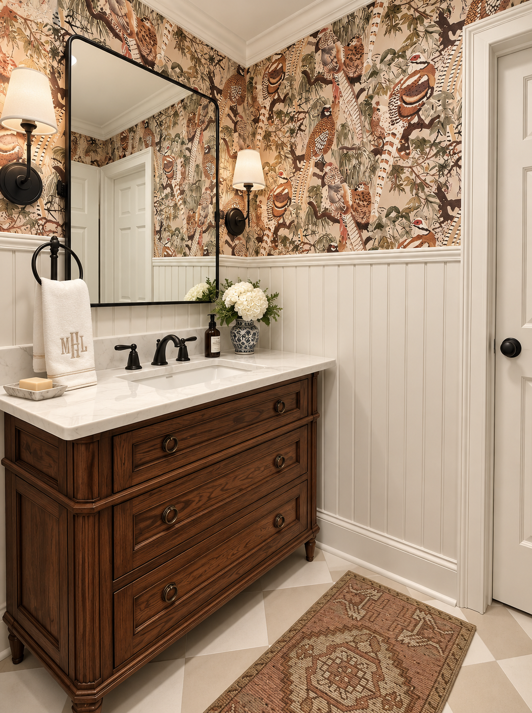 Bathroom with a wooden vanity, white marble countertop, large mirror, wall-mounted light fixtures, floral wallpaper with birds, a vase with white flowers, and a patterned rug.