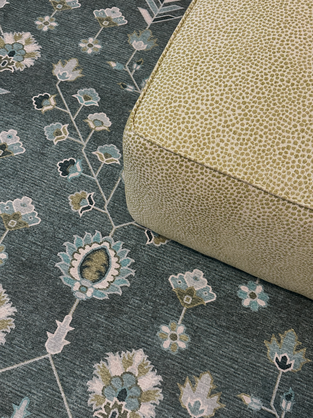 Close-up of a patterned rug with blue, white, and light green floral designs and a beige upholstered piece of furniture.