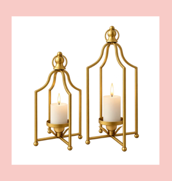 Two gold candle holders with lit white candles on a pink background.