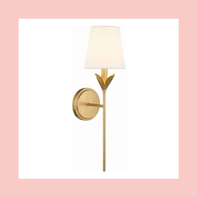 Wall-mounted gold sconce with a tulip-shaped design, featuring a white lampshade on a pink background.