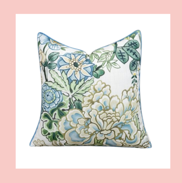 A square decorative pillow with a floral pattern in shades of blue, green, and beige on a white background, framed by a pink border.